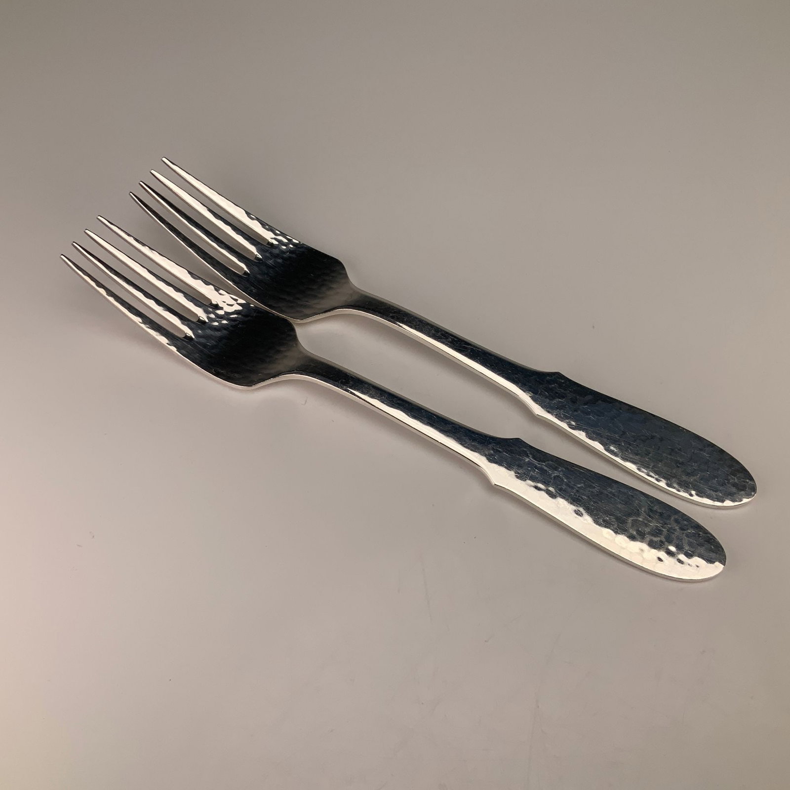 A Pair of Georg Jensen Denmark Mermaid Pattern Hammered Silverplate Forks: A pair of Georg Jensen silver-plated forks in the Mermaid pattern. These pieces are manufactured from electro-plated nickel silver (EPNS) and feature a hand-hammered finish across the handles and the 