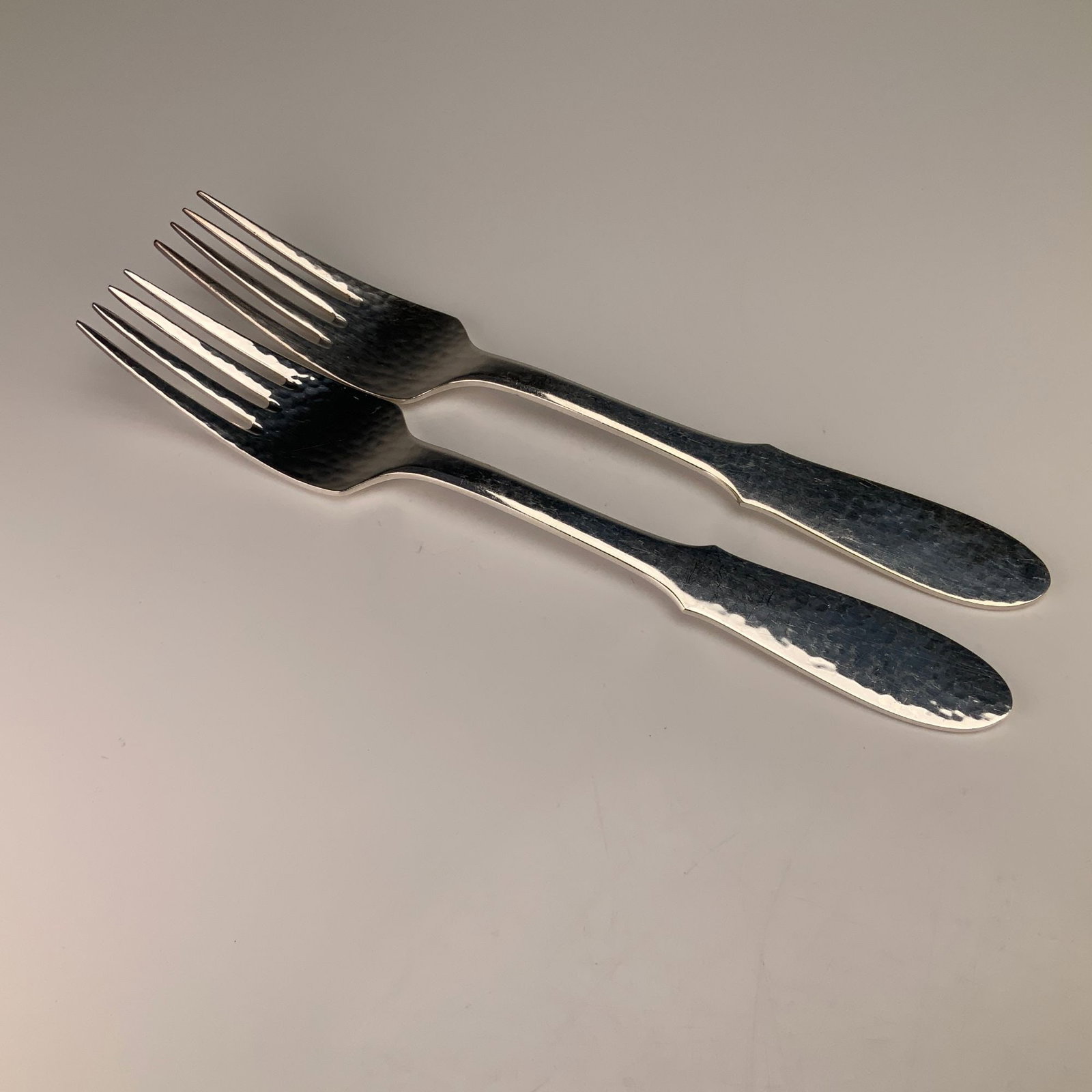 A Pair of Georg Jensen Denmark Mermaid Pattern Silver-Plated Forks: A pair of four-tine forks in the Mermaid pattern by Georg Jensen. These items are constructed from silver-plated nickel silver, indicated by the E.P.N.S. mark. The forks feature a hand-hammered finish