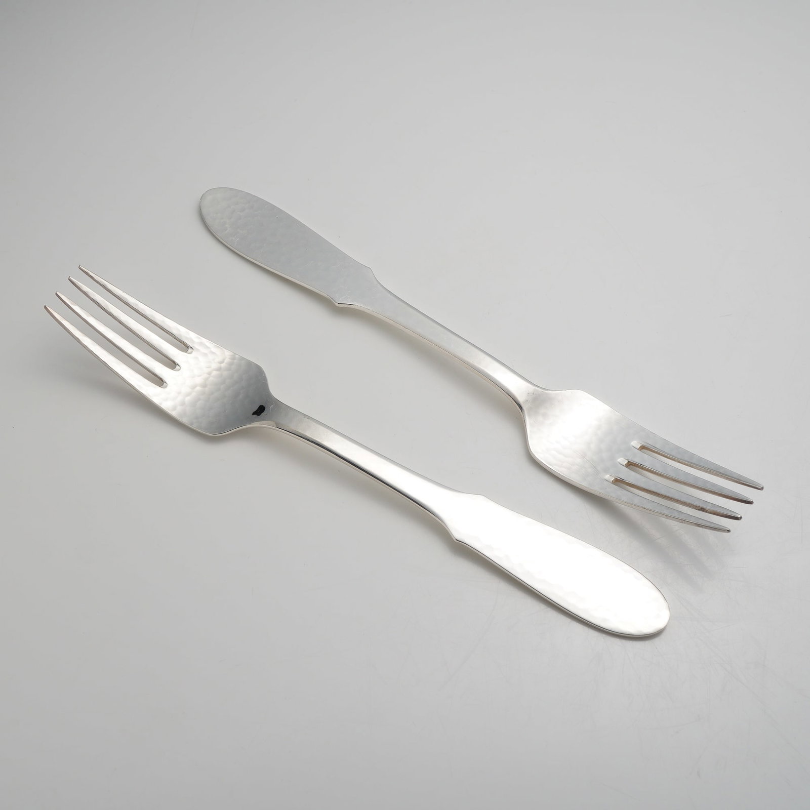 A Pair of Georg Jensen Denmark Mermaid Pattern Silver-Plated Forks: This pair of silver-plated forks is in the Mermaid pattern by Georg Jensen, Denmark. Each fork features a four-tine head with a distinct hammered finish on the front surface. The handles are designed 