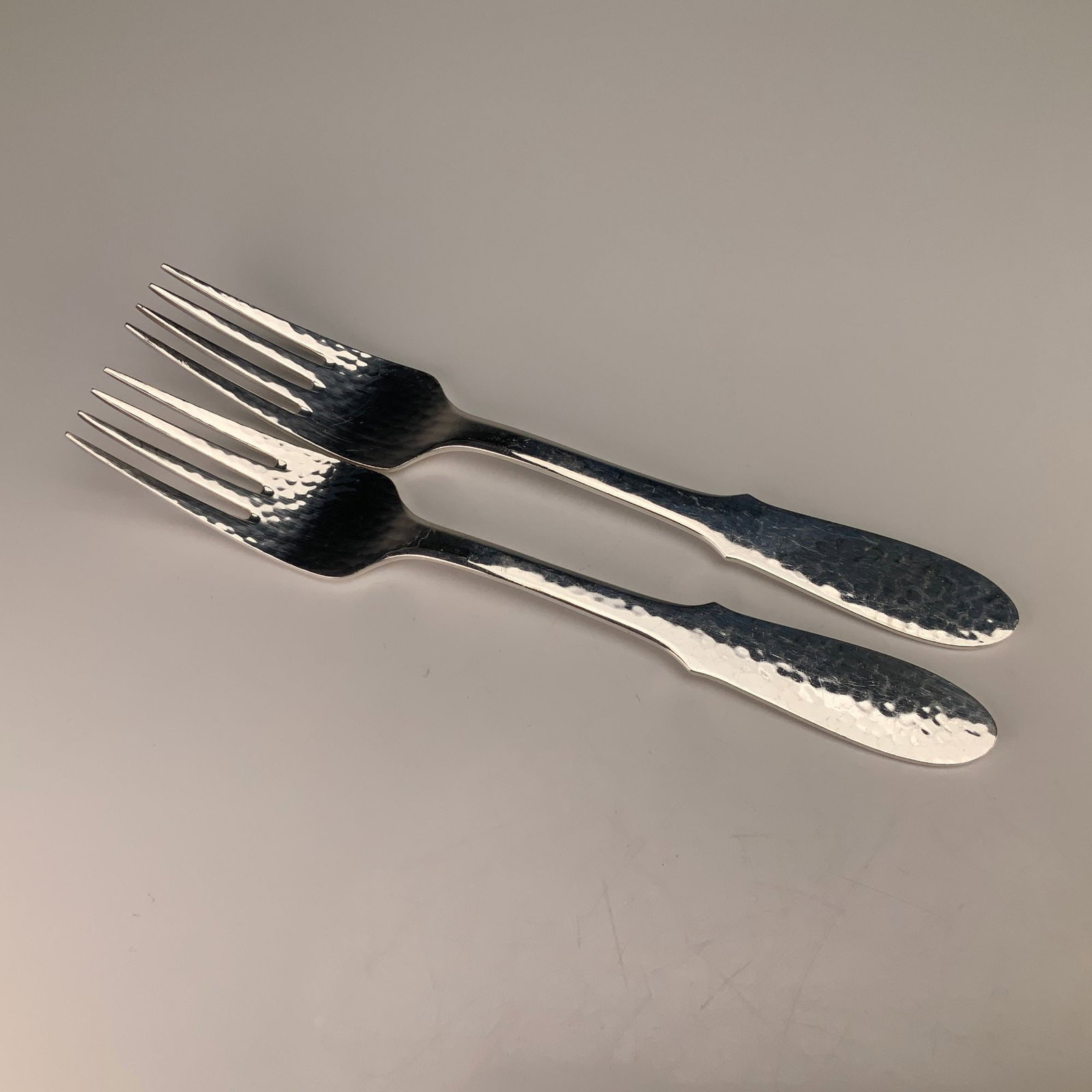 A Pair of Georg Jensen Denmark Mermaid Pattern Silverplate Forks: A pair of silver-plated forks in the Mermaid pattern by Georg Jensen. Each fork features a hand-hammered texture on the front of the fiddle-shaped handle and at the base of the tines. The handles are 