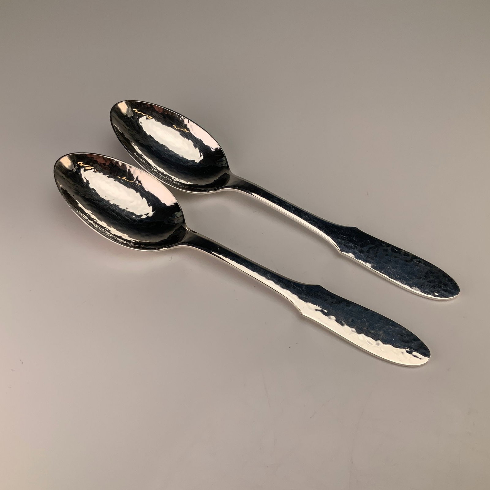 A Pair of Georg Jensen Denmark Mermaid Pattern Silverplate Teaspoons: A pair of silverplated teaspoons in the Mermaid pattern by Georg Jensen. These pieces feature a hand-hammered finish across the oval bowls and the handles. The handles are designed with a flared, shap