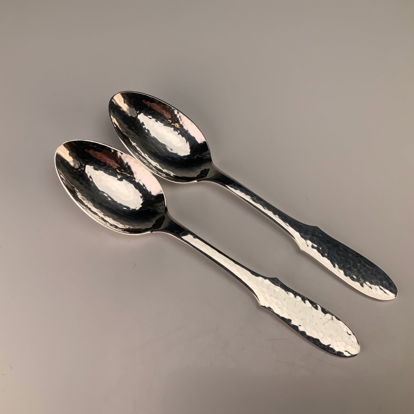 A Pair of Georg Jensen Mermaid Pattern Hammered Silverplate Teaspoons: A pair of Georg Jensen silver-plated teaspoons in the Mermaid pattern. Each spoon features a hand-hammered finish across the interior of the bowl and the handle. The handles are designed in a spatulat