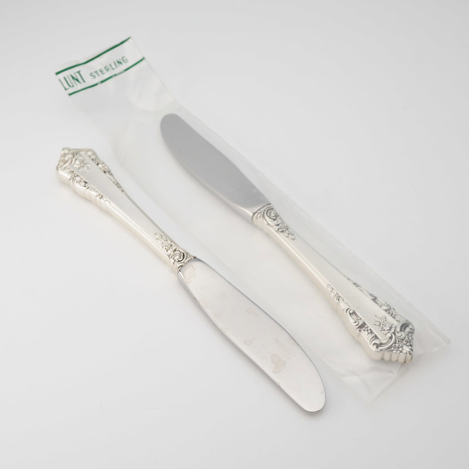2pc Lunt Sterling Silver and Stainless Steel Butter Spreaders Knives, Rondelay: A pair of Lunt Silversmiths butter spreaders in the ornate Rondelay pattern, first introduced in 1963. These pieces feature hollow sterling silver handles with stainless steel blades. The design is ch