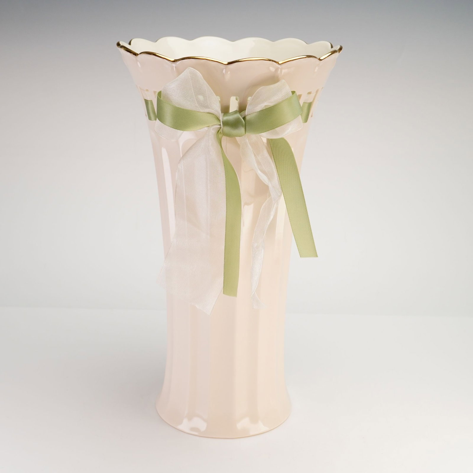 Lenox Beloved Vase, Love Notes: Ivory-color porcelain vase designed for long-stemmed floral arrangements. The body features a pierced and fluted surface with green ribbon and tulle motifs forming a bow detail. The rim is scalloped w