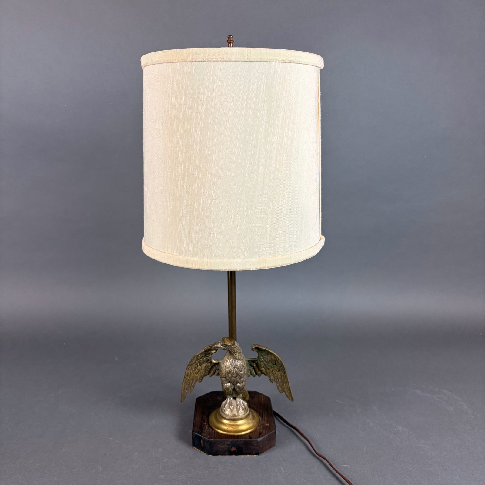 American Federal Style Cast Metal Eagle Table Lamp on Wooden Base: This table lamp is designed in the American Federal style, featuring a cast metal eagle with spread wings as the primary decorative element. The eagle figure is finished in a brass tone and is mounted