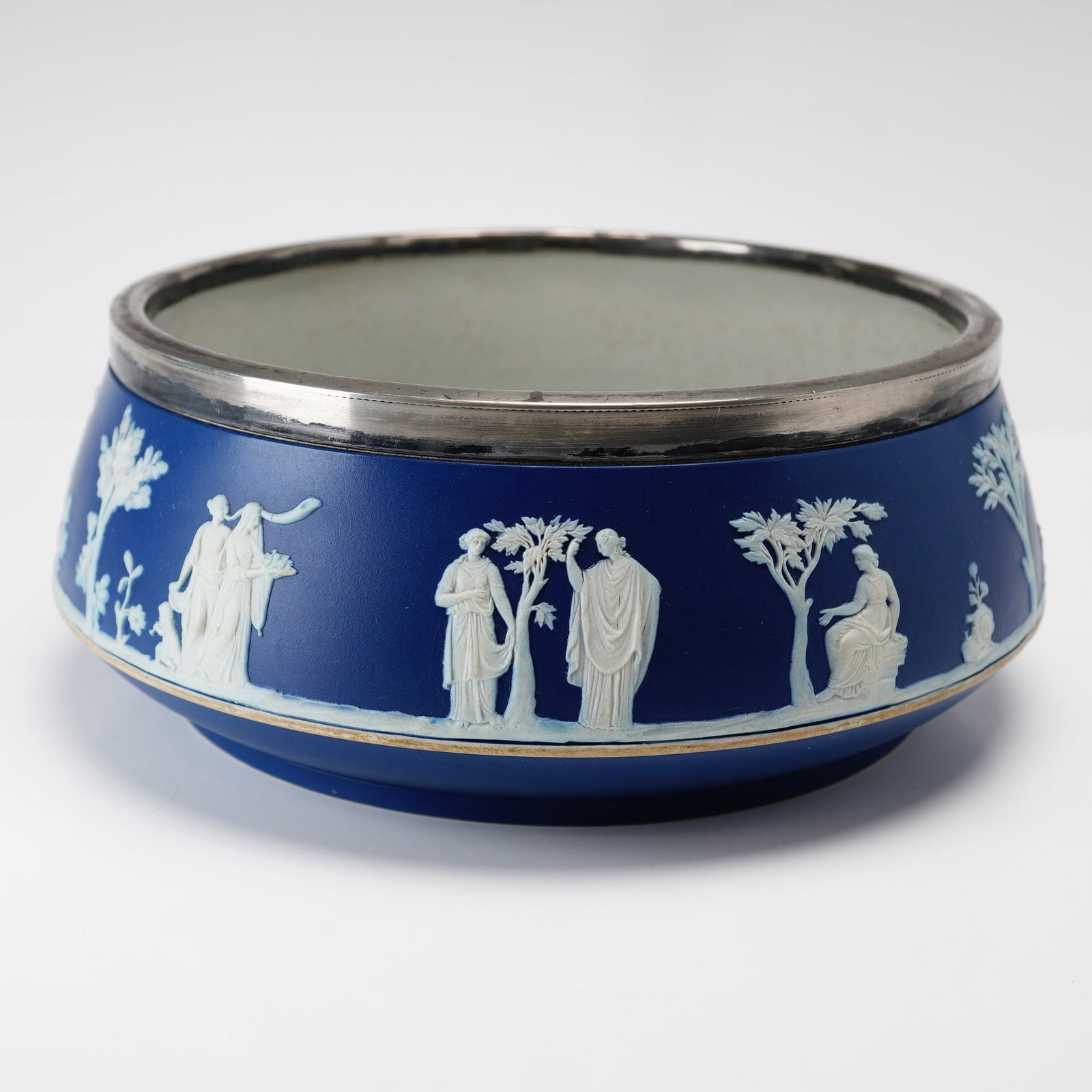 Wedgwood Cobalt Blue Jasperware Bowl with Silverplate Rim: This Wedgwood jasperware bowl features a matte cobalt blue stoneware body with cream colored sprigged relief decoration. The exterior is ornamented with a continuous neoclassical frieze depicting vari