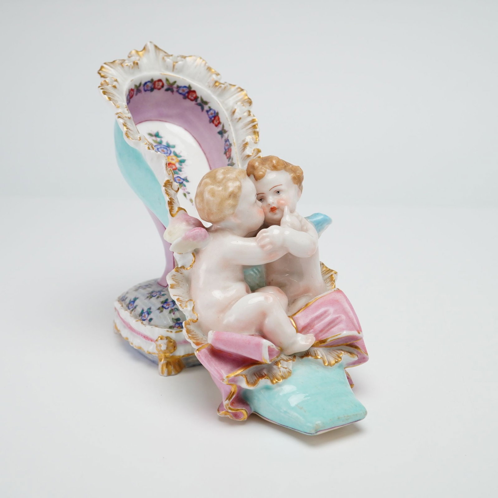 Meissen Porcelain Figurine of Cherubs in a Shoe: A Meissen glazed and hand-painted porcelain ornamental figurine featuring two cherubs in a shoe. The composition depicts two playful putti seated within a decorative high-heeled slipper. The slipper i