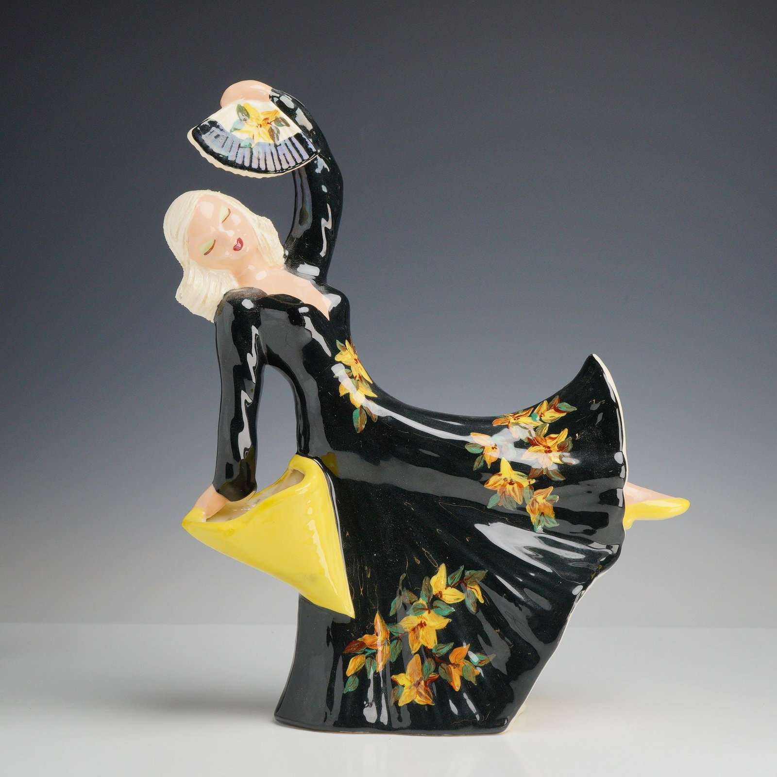 Hedi Schoop Hollywood Gal Figurine with Black Floral Dress and Fans: This glazed ceramic figurine is the Hollywood Gal model by Hedi Schoop. The Mid-Century Modern figure is depicted in a dynamic dancing pose, holding a decorated fan above her head with her right hand 