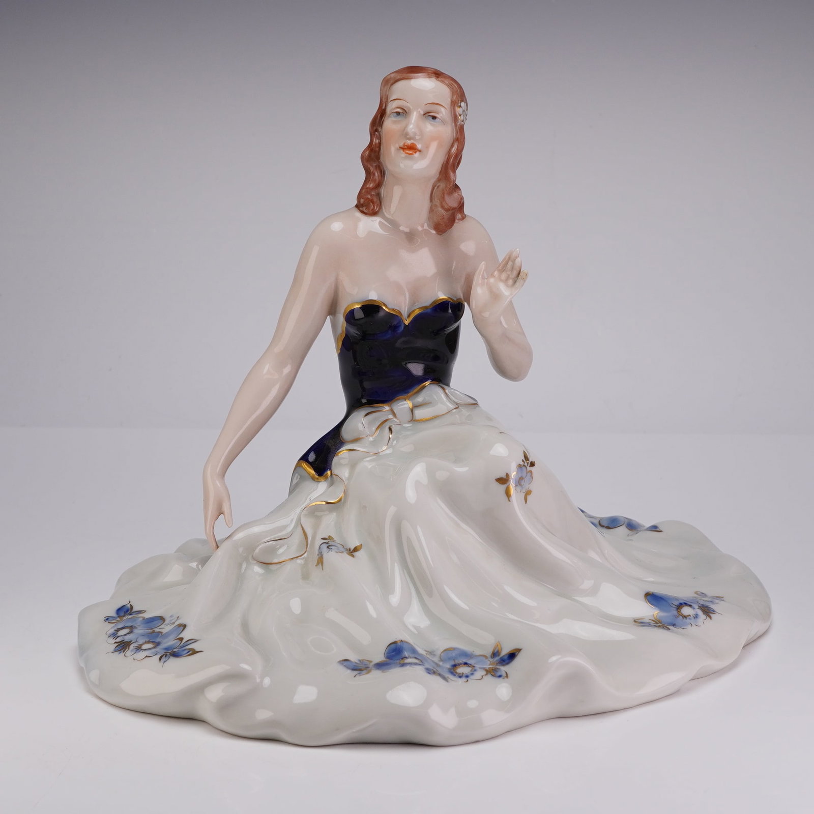 Royal Dux Bohemia Porcelain Seated Elegant Lady Figurine: A mid-20th-century glazed porcelain figurine manufactured by Royal Dux Bohemia. The figure depicts a seated woman with auburn hair in a theatrical pose, wearing a strapless cobalt blue bodice with gil