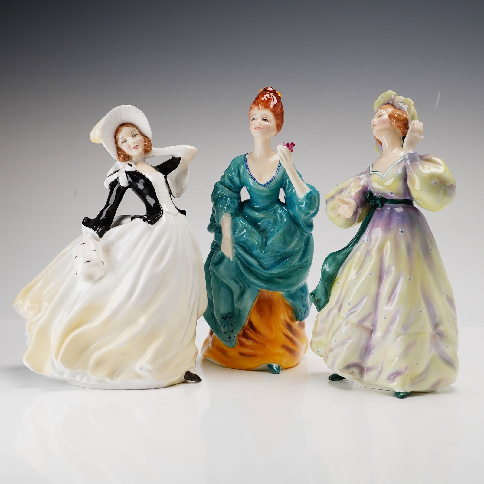 Three Royal Doulton Figurines- Autumn Breezes HN2147, Olga 2463, and Grand Manner 2723: This collection of rdf x 3 hand-painted glazed porcelain and bone china figurines is produced by Royal Doulton. The group features three women in stylized period dress from the company HN series. The 