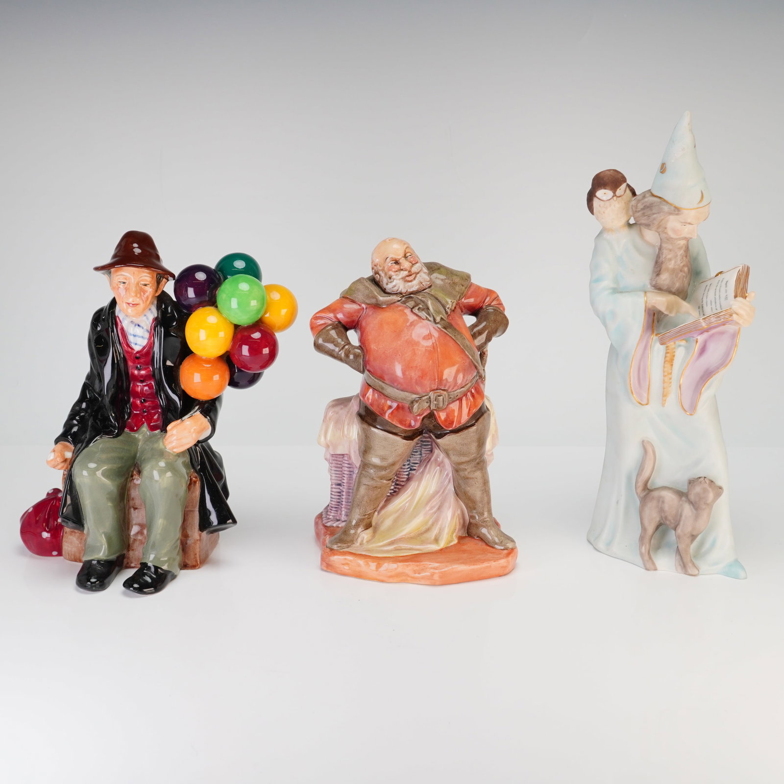 3pc Royal Doulton Figurines, Falstaff HN2054, Balloon Man 1954 & Wizard 4069: This collection consists of three glazed porcelain figurines produced by Royal Doulton in England. The first item is titled The Balloon Man, model HN 1954. It depicts a seated male figure in a brown h