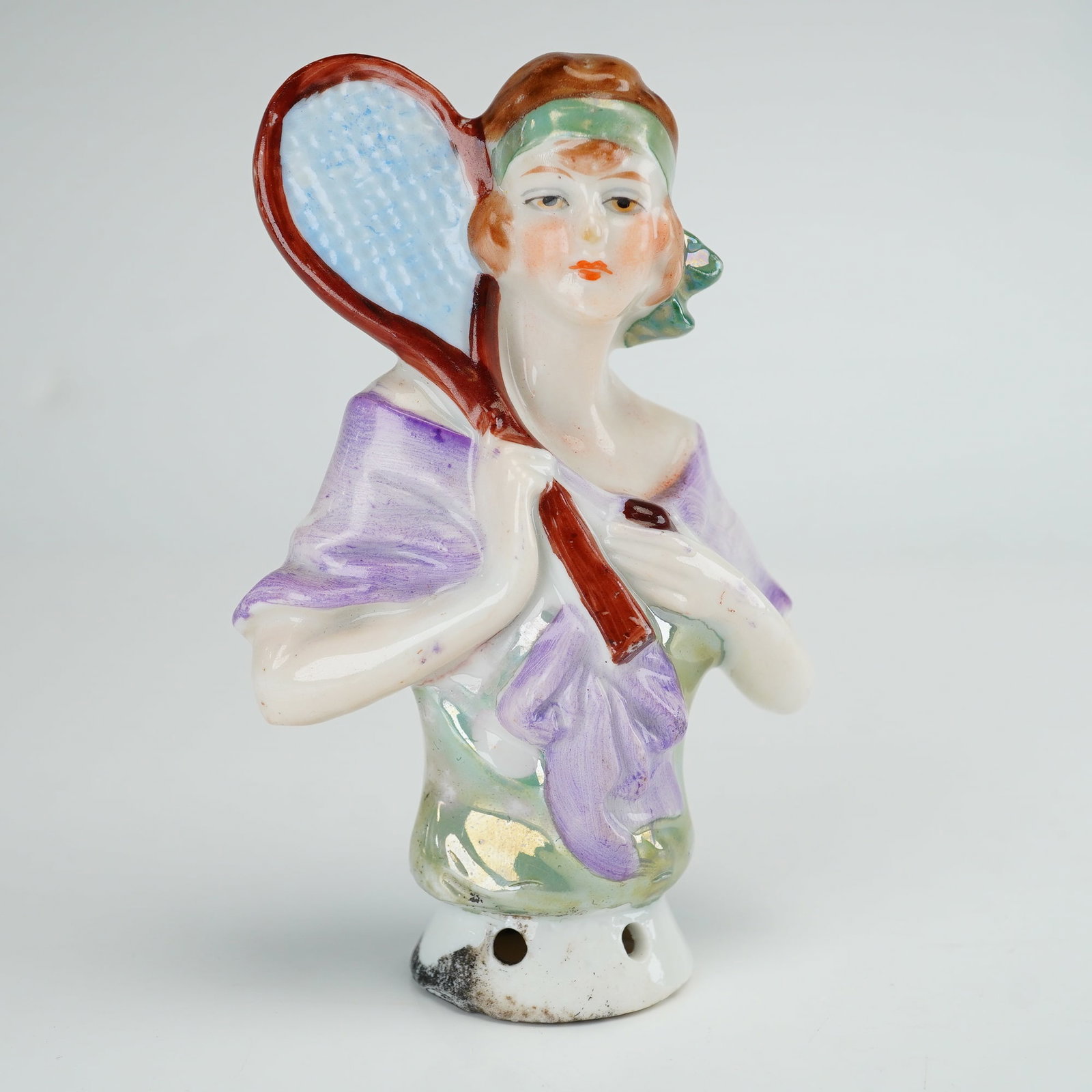 Art Deco Porcelain Tennis Player Half Doll, Germany: This Art Deco period porcelain half doll depicts a female tennis player in a stylized flapper aesthetic. The figure features bobbed brown hair secured with a green headband and is draped in a purple s