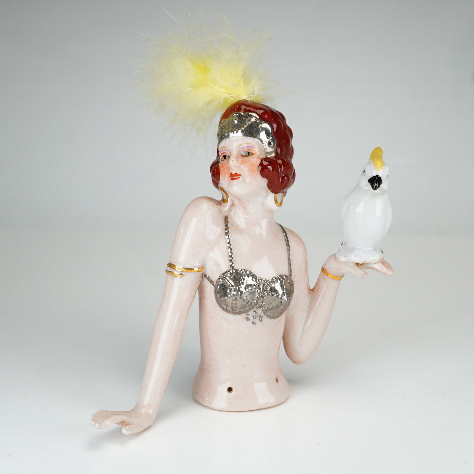 German Art Deco Mata Hari Porcelain Half Doll with Cockatoo and Feather: This German Art Deco glazed porcelain half doll is modeled in the Mata Hari pattern, depicting a cabaret-style performer in a stylized pose. The figure features hand-painted facial features and an aub