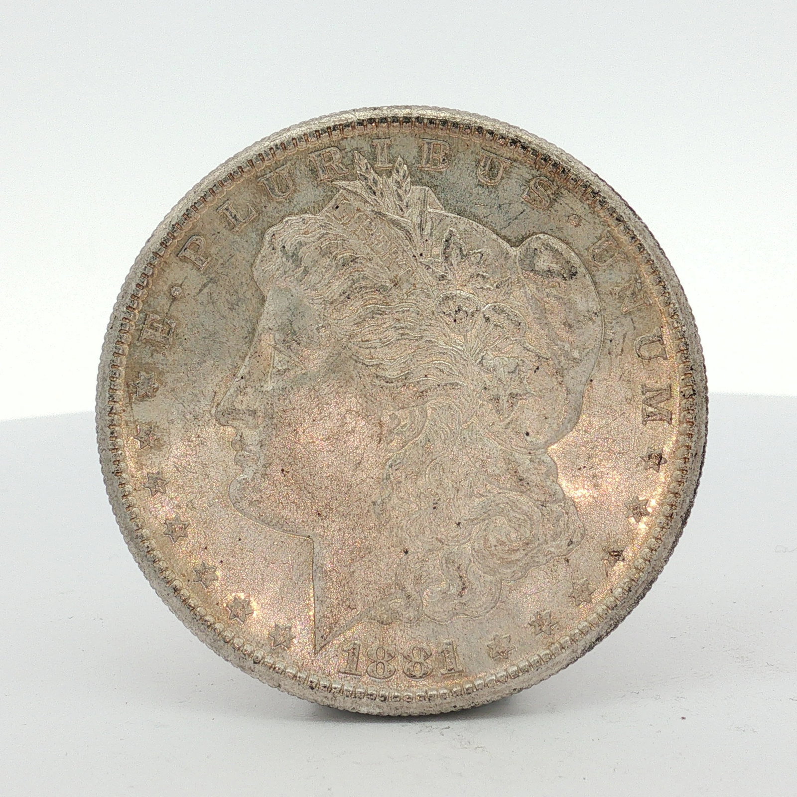 1881-S US One Dollar Morgan Silver Dollar, Circulated: This US silver coin is a Morgan dollar struck at the San Francisco Mint. The piece features a reeded edge and is composed of 0.900 fine silver and 10 percent copper. The obverse bears the inscription 