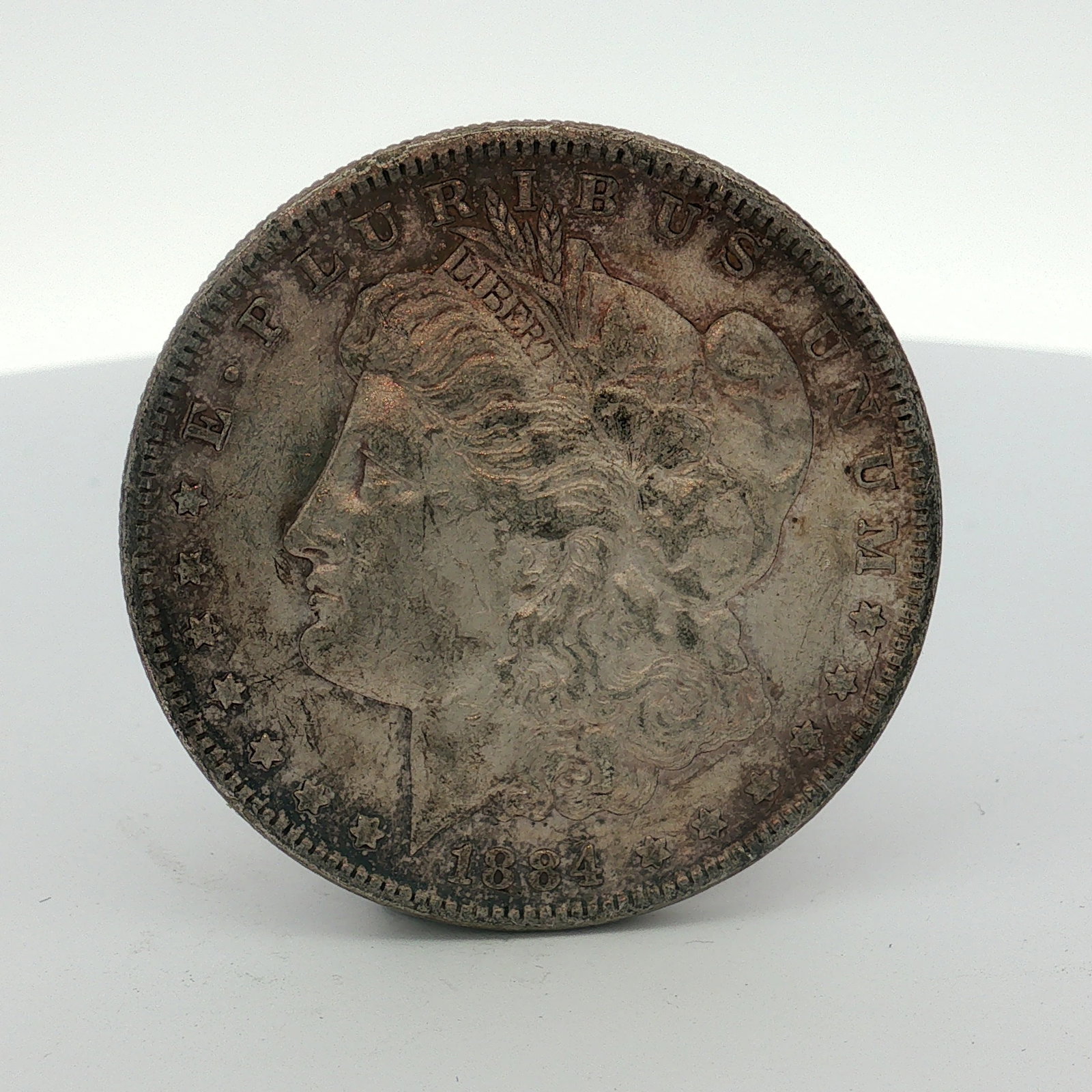 1884 US One Dollar Morgan Silver Dollar, Circulated: This coin was struck at the Philadelphia Mint and is composed of .900 fine silver and .100 copper. It features the Morgan dollar design type. The no mint mark is located on the reverse above the denom