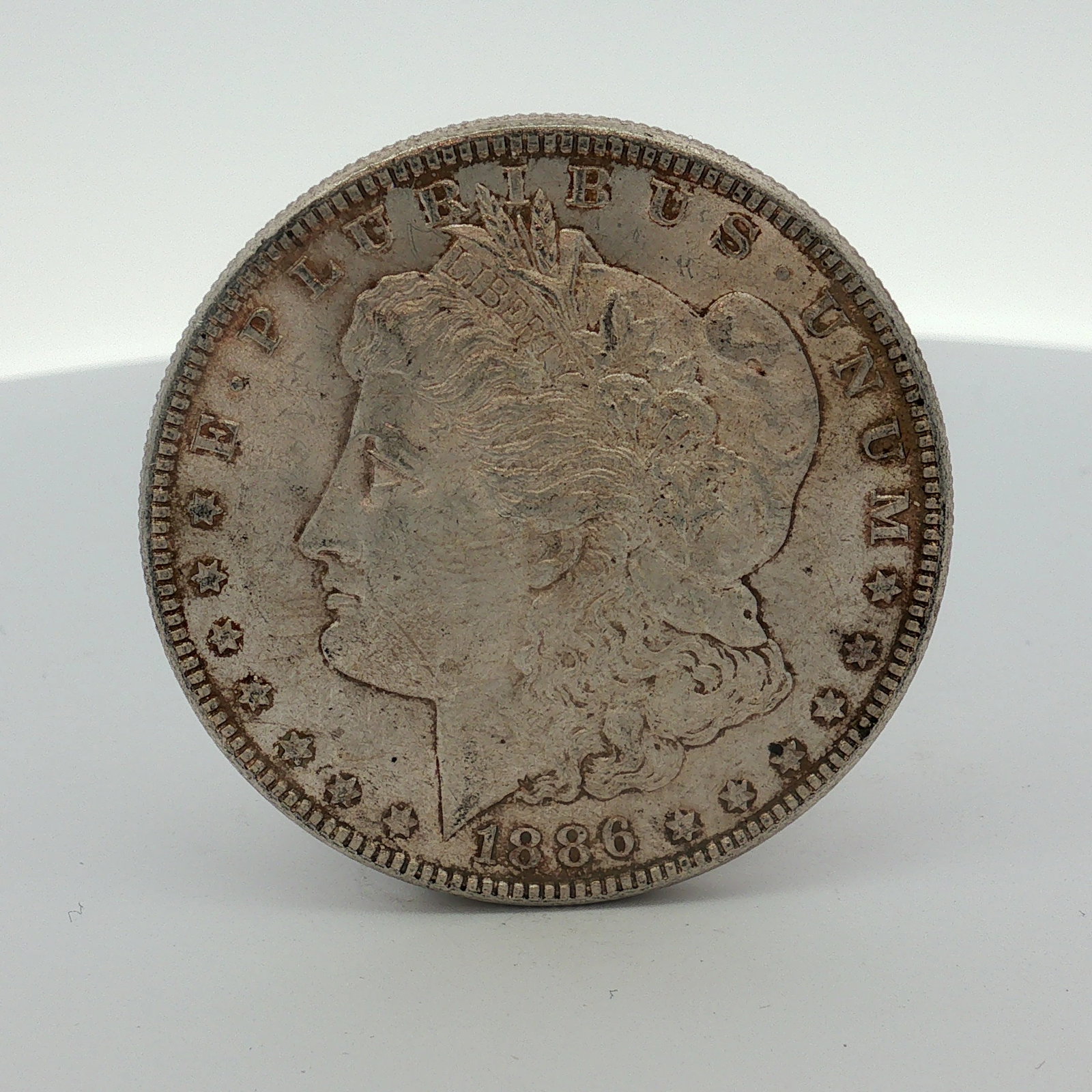 1886 US Morgan Silver Dollar Coin Circulated: This 1886 US Morgan dollar was struck at the Philadelphia mint. The coin is composed of 90% silver and 10% copper with a reeded edge. It features the Liberty Head obverse and the heraldic eagle revers