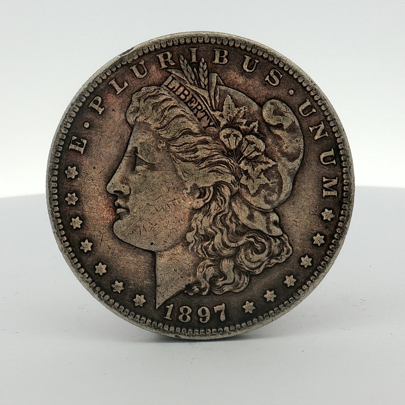 1897-S US One Dollar Morgan Silver Dollar, Circulated: This US 1897-S Morgan silver dollar was struck at the San Francisco Mint. The coin features the Morgan dollar obverse and reverse designs. The obverse is inscribed with E PLURIBUS UNUM and the date 18