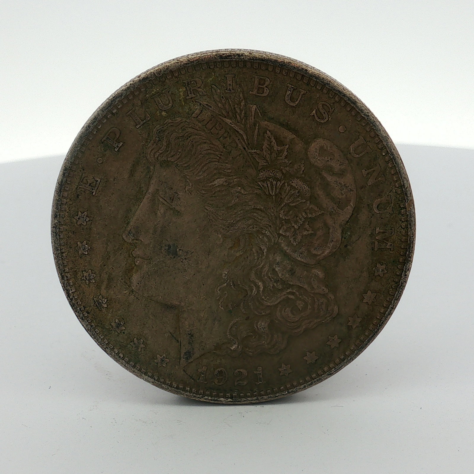 1921 US One Dollar Morgan Silver Dollar, Circulated: This US 1921 Morgan silver dollar was struck at the Philadelphia Mint. The coin is composed of 90 percent silver and 10 percent copper and features a reeded edge. The obverse displays the Morgan desig
