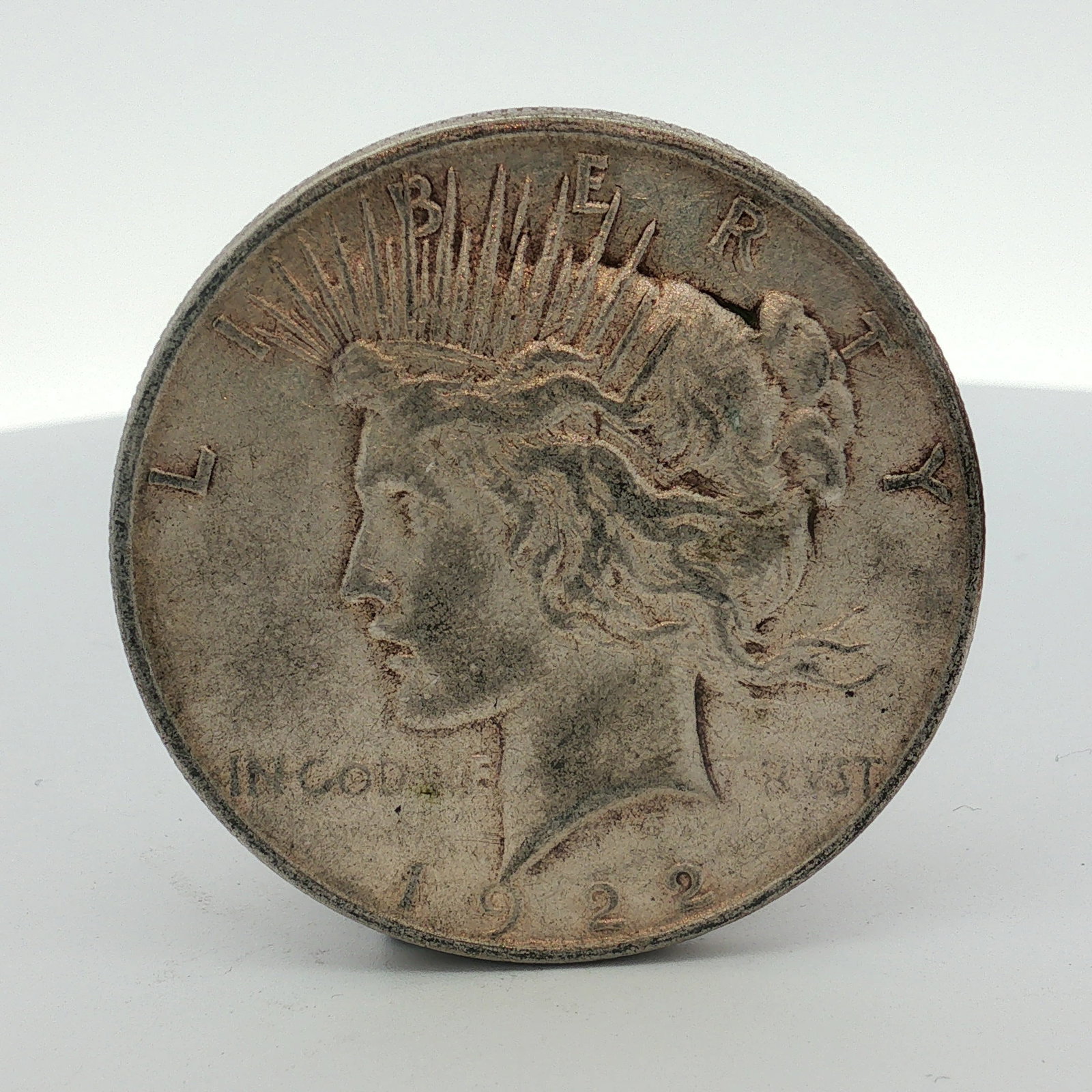 1922-D US One Dollar Peace Silver Dollar, Circulated: This 1922-D US Peace silver dollar is a circulating-issue coin struck at the Denver Mint. The coin is composed of 90% silver and 10% copper. The obverse features the Liberty design with inscriptions L