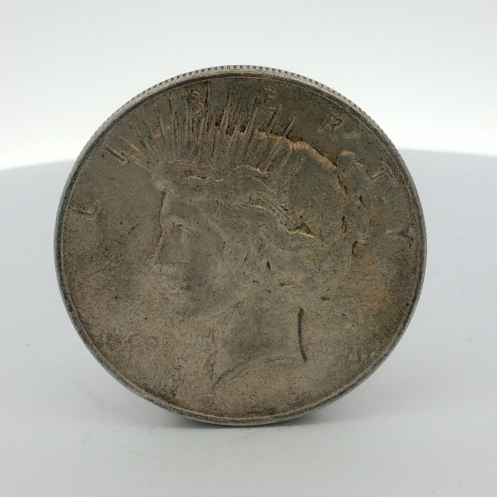 1926-D US One Dollar Peace Silver Dollar, Circulated: This US Peace dollar is a Denver-minted coin struck in silver. The specimen features the standard Peace dollar design type with a reeded edge. Obverse inscriptions include LIBERTY, IN GOD WE TRVST, an