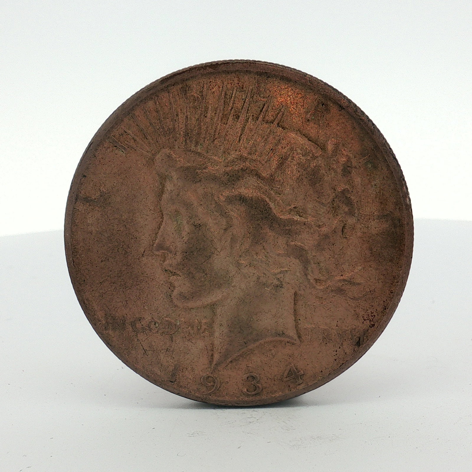 1934-D US One Dollar Silver Peace Dollar, Circulated: This Denver Mint issue features a reeded edge with a D mint mark below the O on reverse. The coin is characterized by a non-standard, deep reddish-brown to copper-colored surface oxidation across both