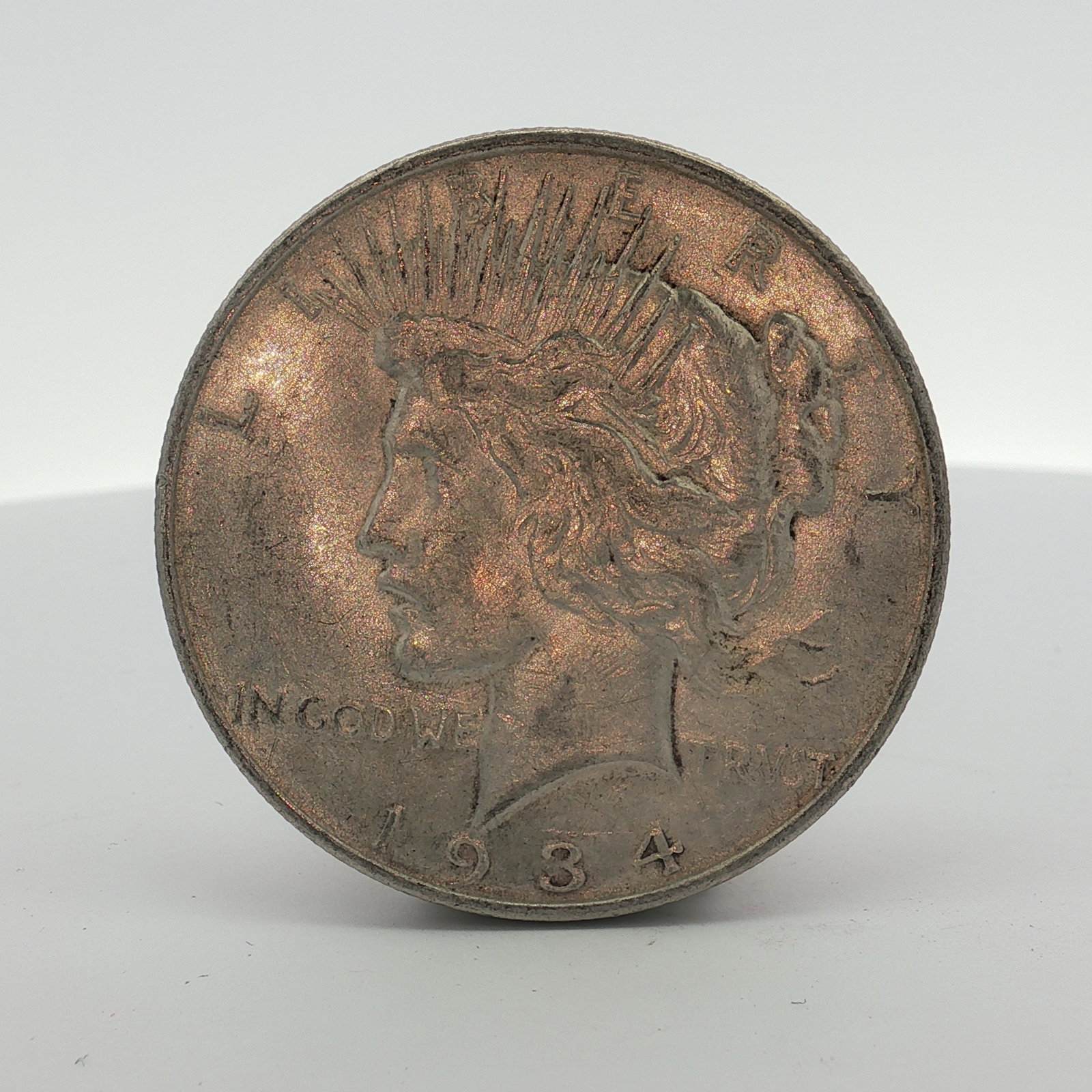1934-D US One Dollar Silver Peace Dollar, Circulated: This US silver coin is a Peace dollar struck at the Denver Mint. The obverse features the Peace dollar design and is dated 1934. The reverse displays the D mint mark located to the left of the tail fe