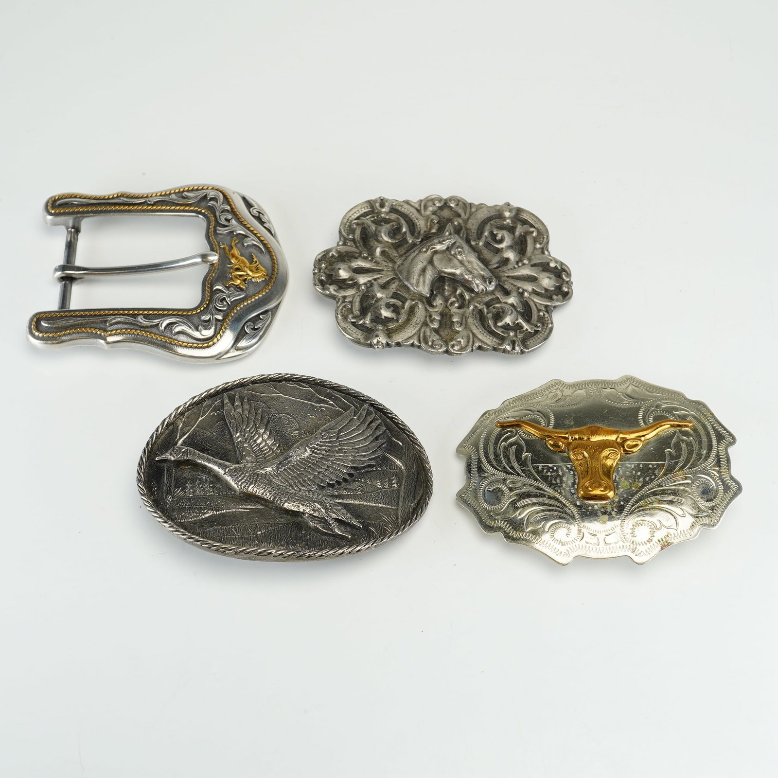 4pc Collection of Western and Wildlife Metal Belt Buckles including Bergamot Brass Works: This collection of metal belt buckles features various Western and wildlife motifs. Included is an equestrian buckle by Bergamot Brass Works, featuring a central horse head in profile surrounded by ac
