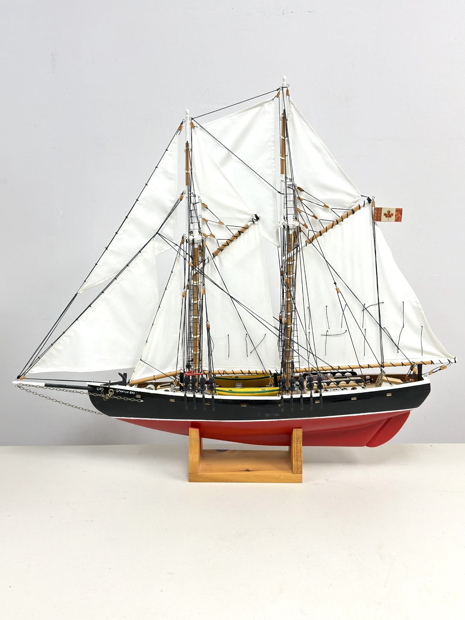 Handcrafted Wooden Model Schooner Spanish Bay with Display Stand: Handcrafted wooden scale model of a two-masted schooner, bearing the name Spanish Bay. The vessel is constructed with a carved wood hull featuring a red-painted bottom, a black topside, and a white