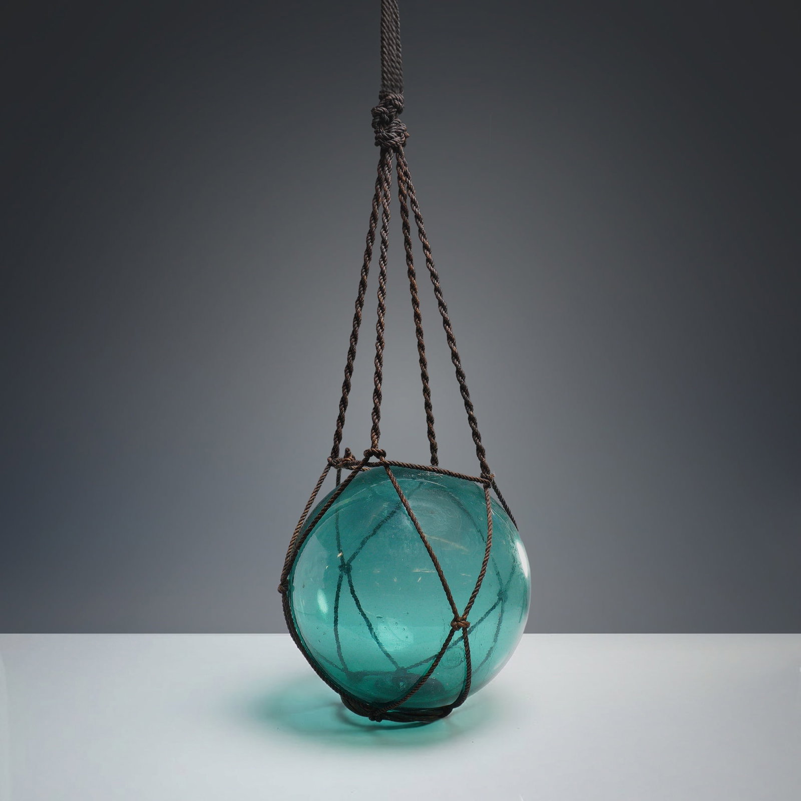 Vintage Japanese Blue Glass Fishing Net Buoy: This hand-blown glass fishing buoy floating roped ball, also known as an ukidama or bindama, is attributed to Japanese maritime production from the mid-20th century. The spherical buoy is made of tran