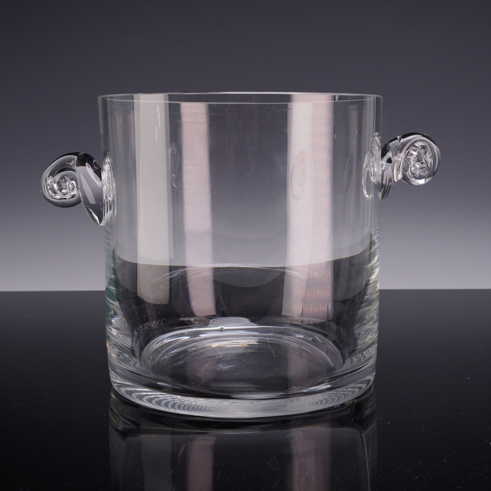 Tiffany and Co. Crystal Scroll Handled Ice Bucket: A heavy, cylindrical ice bucket crafted from clear lead crystal by Tiffany and Co. The vessel features a thick, polished base and two hand-applied, scroll-form handles positioned on opposite sides. Th