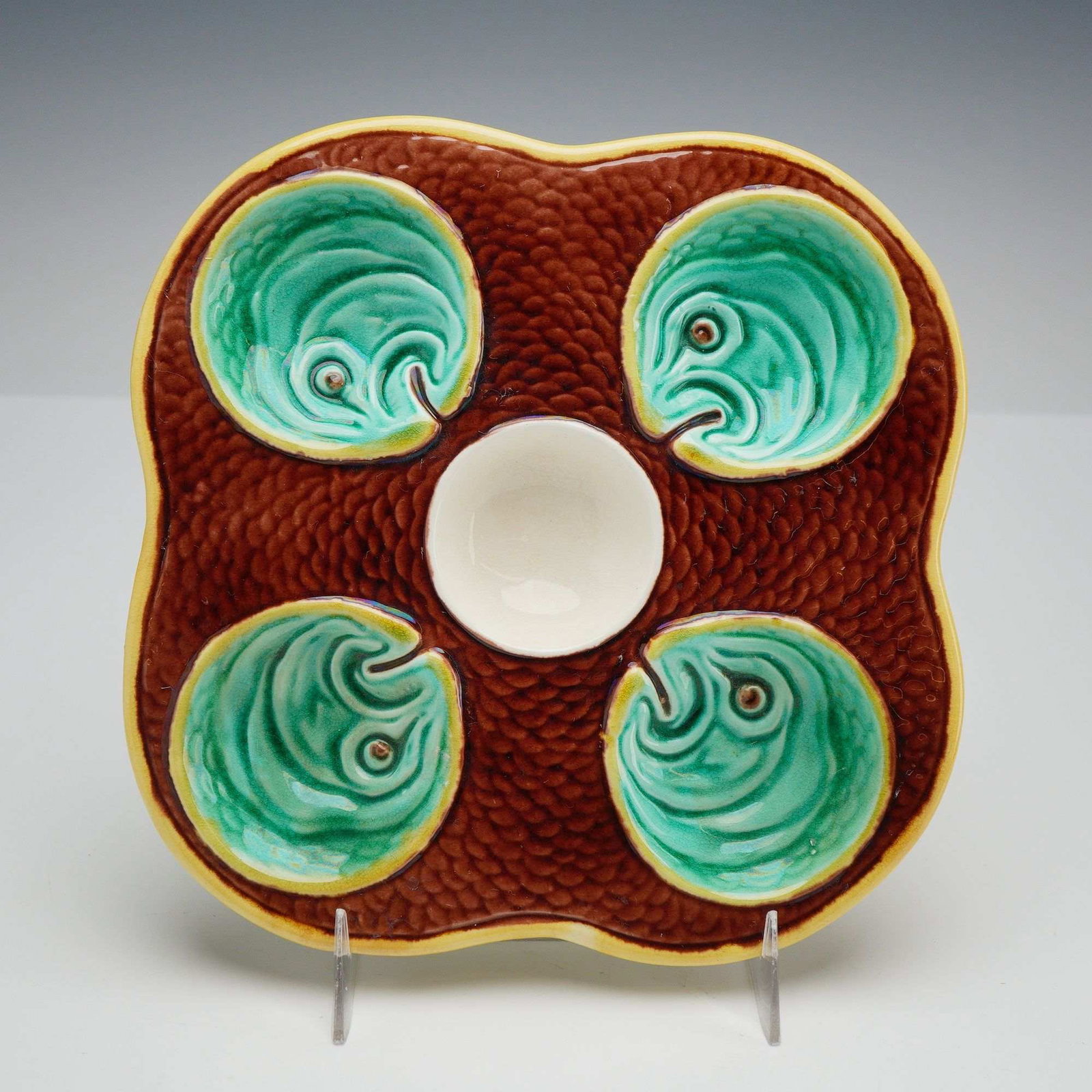 Wedgwood Majolica Fish Heads on Scales Oyster Plate: A lead-glazed earthenware majolica oyster plate produced by Wedgwood, sourced from the Rubin Collection. The plate features a square form with rounded, scalloped corners. The surface is organized with