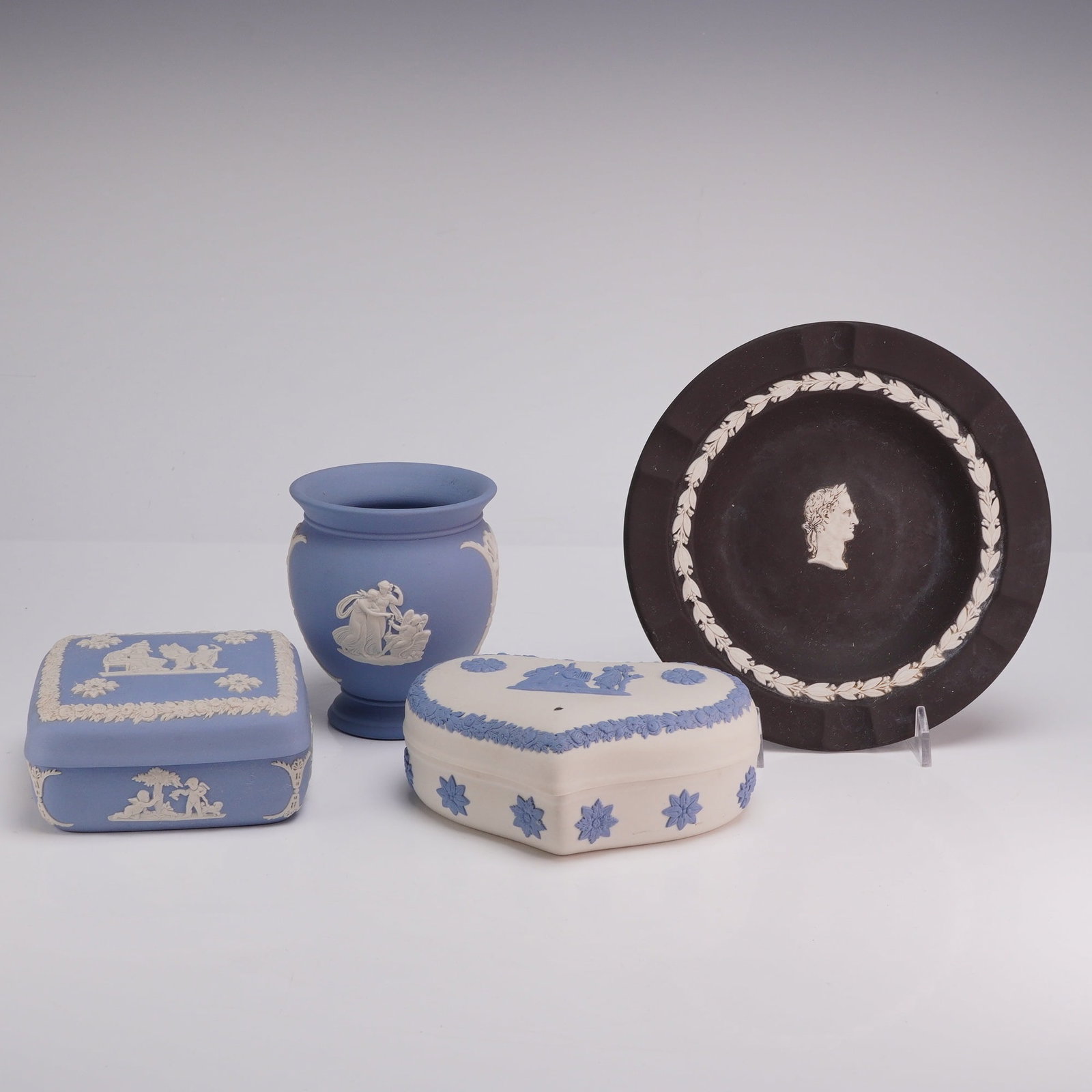 4pc Wedgwood Jasperware Lidded Boxes, Vase and Plate: This collection of Wedgwood Jasperware items is crafted from English matte-finish stoneware featuring applied bas-relief sprigging. The group includes a circular black jasperware plate or dish with a 
