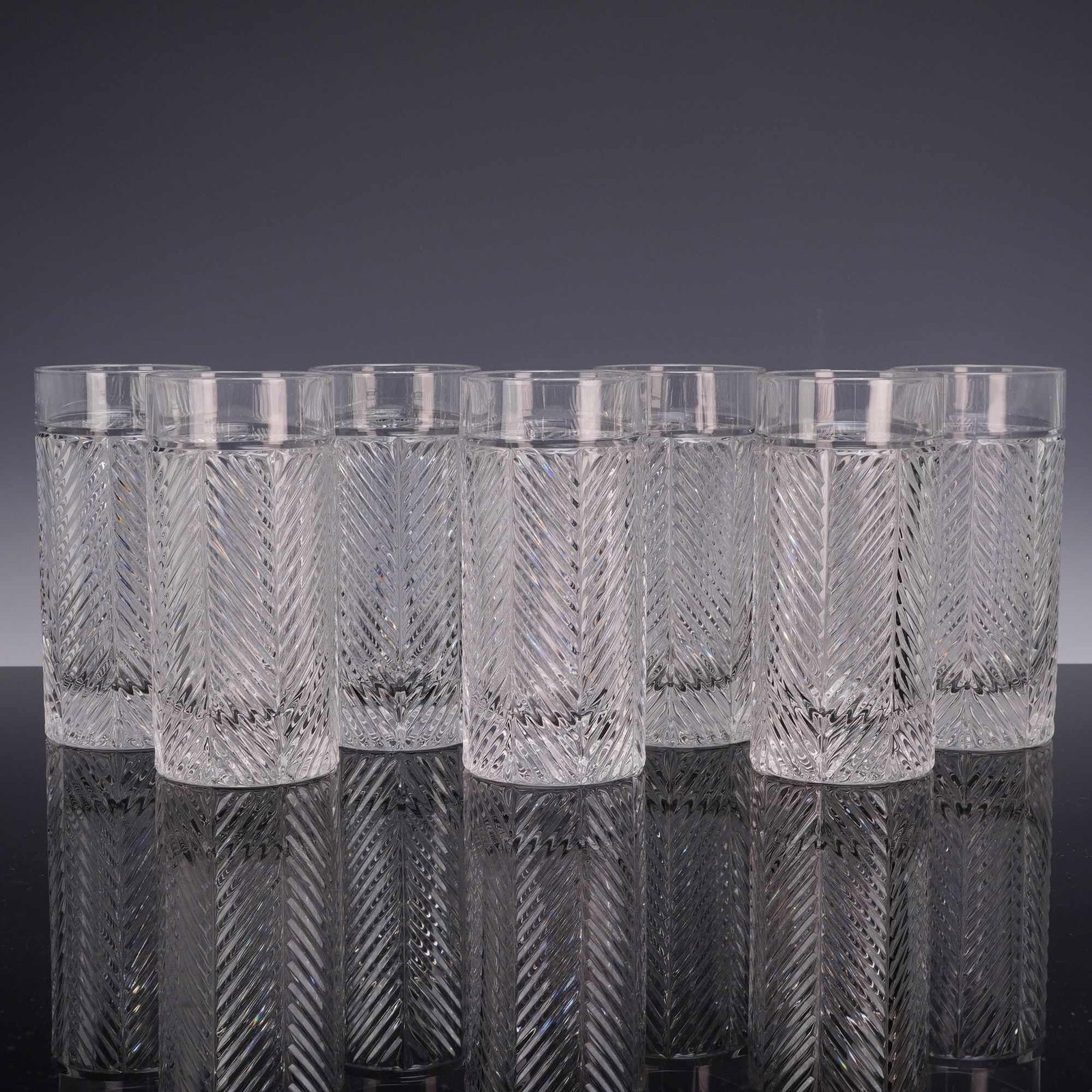 A Set of Seven Ralph Lauren Herringbone Crystal Highball Glasses: A set of seven crystal highball glasses in the Herringbone pattern by Ralph Lauren. Each glass features a cylindrical form decorated with multiple vertical columns of deeply cut herringbone facets. Th