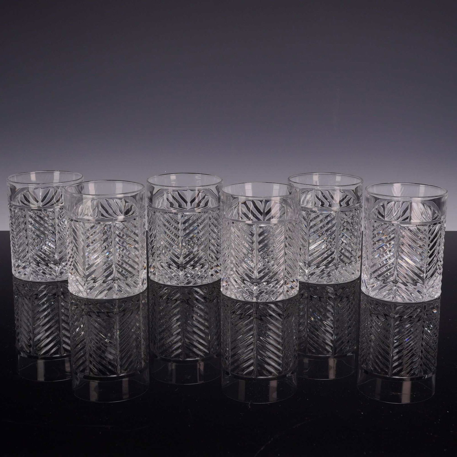 A Set of Six Ralph Lauren Herringbone Crystal Double Old-Fashioned Glasses: This set of six double old-fashioned glasses is crafted from crystal in the Herringbone pattern by Ralph Lauren. Each glass features a heavy, thick base and a deep-cut decorative motif consisting of r