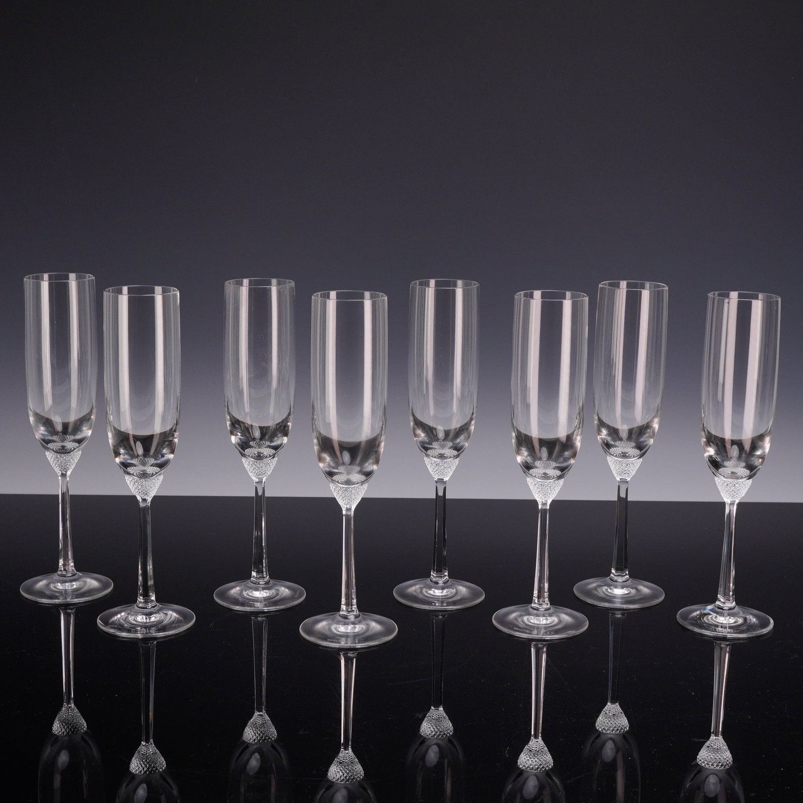 Set of Eight Villeroy & Boch Octavie Crystal Champagne Flutes: This set of eight Villeroy & Boch champagne flutes is produced in the Octavie pattern. Each glass is constructed from colorless crystal and features a tall, slender cylindrical bowl. At the junction o