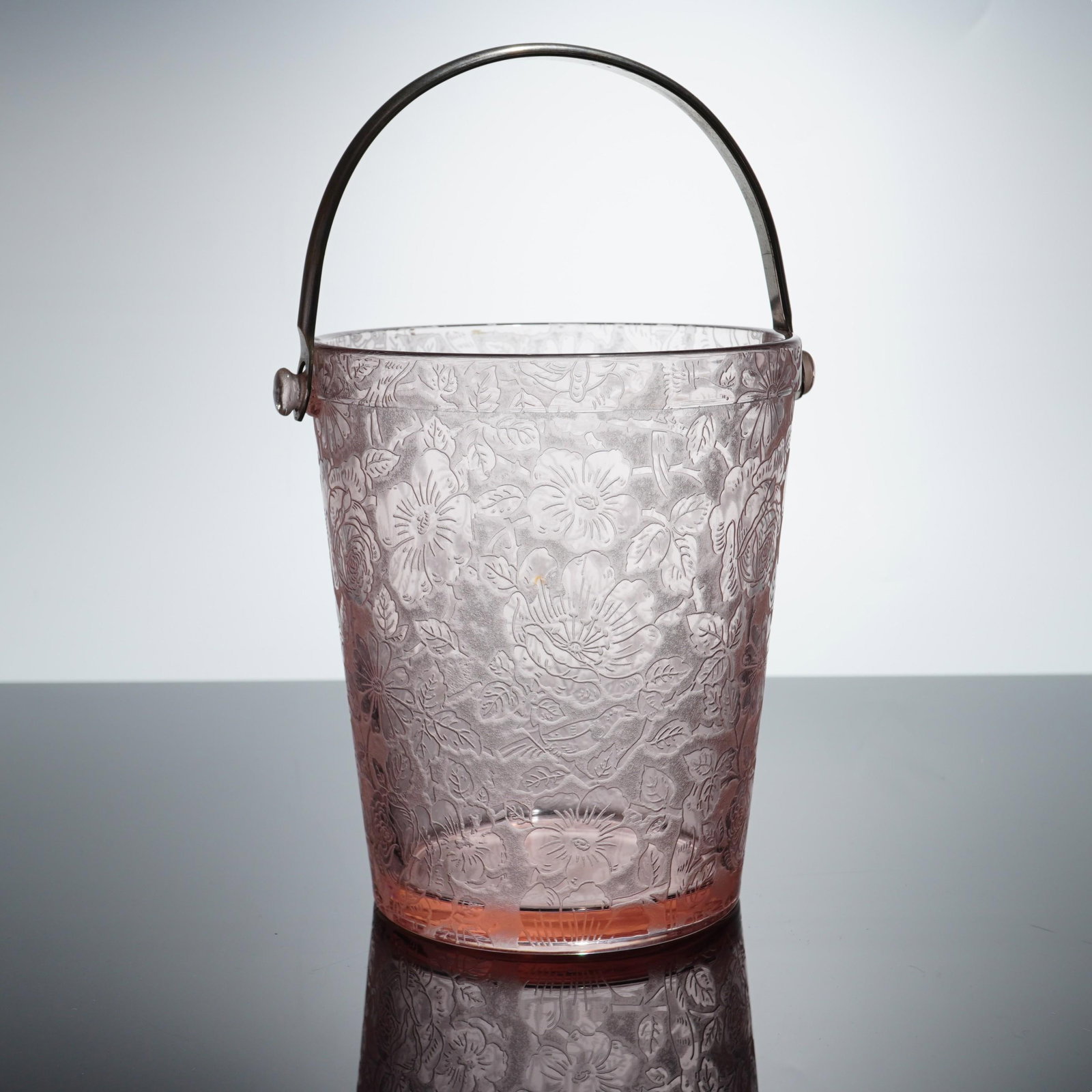 Cambridge Glass Pink Apple Blossom Ice Bucket with Metal Handle: This vintage ice bucket is crafted from pink translucent glass in the Apple Blossom pattern, produced by Cambridge Glass. The vessel features a tapered cylindrical form with a molded decorative motif 