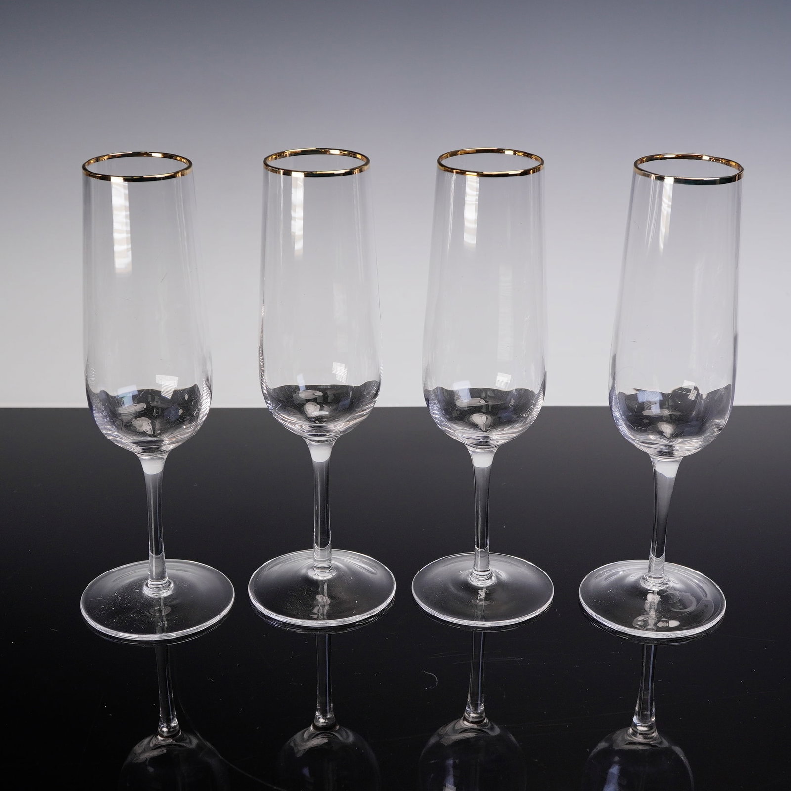 4pc Martha Stewart Champagne Glass Set with Gold Rim: Set of four clear glass champagne flutes, each featuring a slender stem and elongated bowl. The glasses are accented with a gold band around the rim. Dimensions 3"W x 9"H