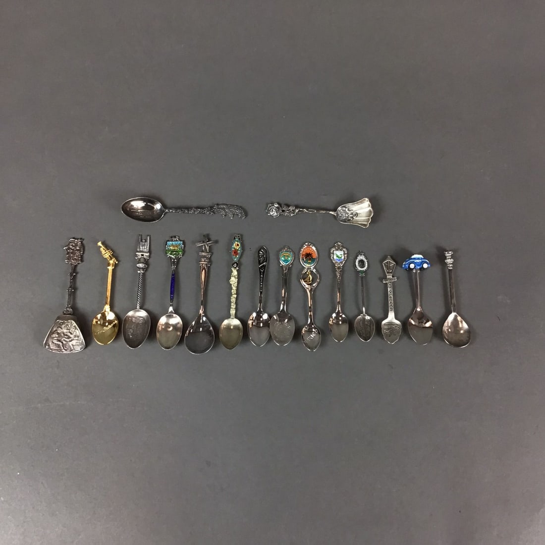 16pc Collection Sterling Silver and Silverplated Souvenir Spoons: Souvenir spoons features a variety of travel-related themes and figural designs. The group includes a gold-tone spoon with a trumpet-shaped handle and a bowl inscribed New Orleans, a spoon with a