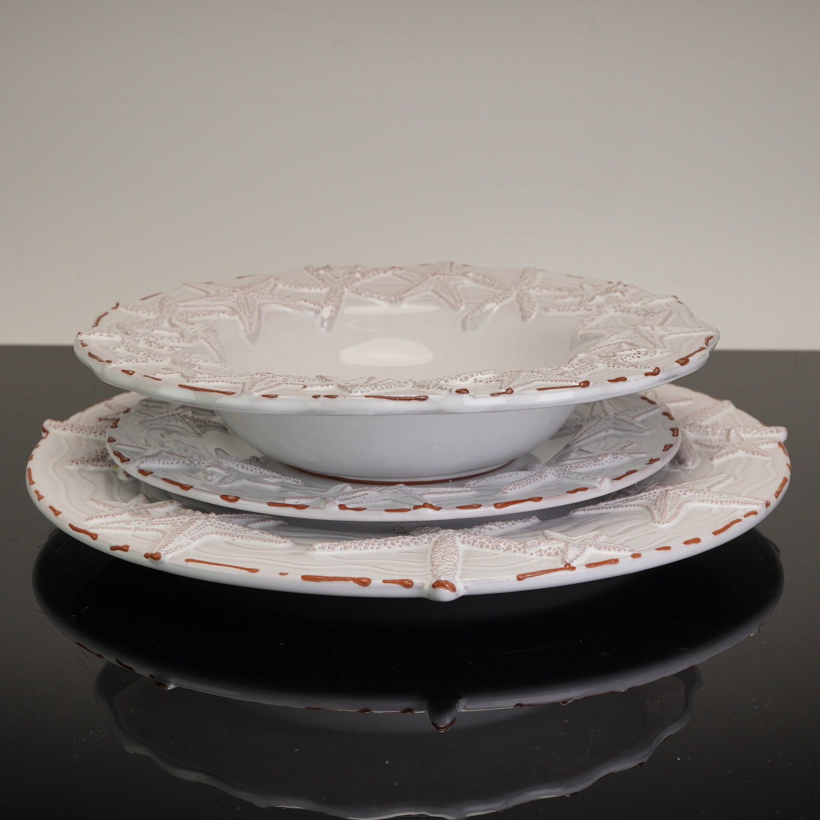 Mud Pie Sanibel Three-Piece Starfish Dinner Plate, Dessert Plate, and Soup Bowl: A three-piece ceramic table setting produced by Mud Pie in the Sanibel pattern. This coastal-themed set is crafted from earthenware with a reddish-brown terracotta body visible at the foot rims and ed