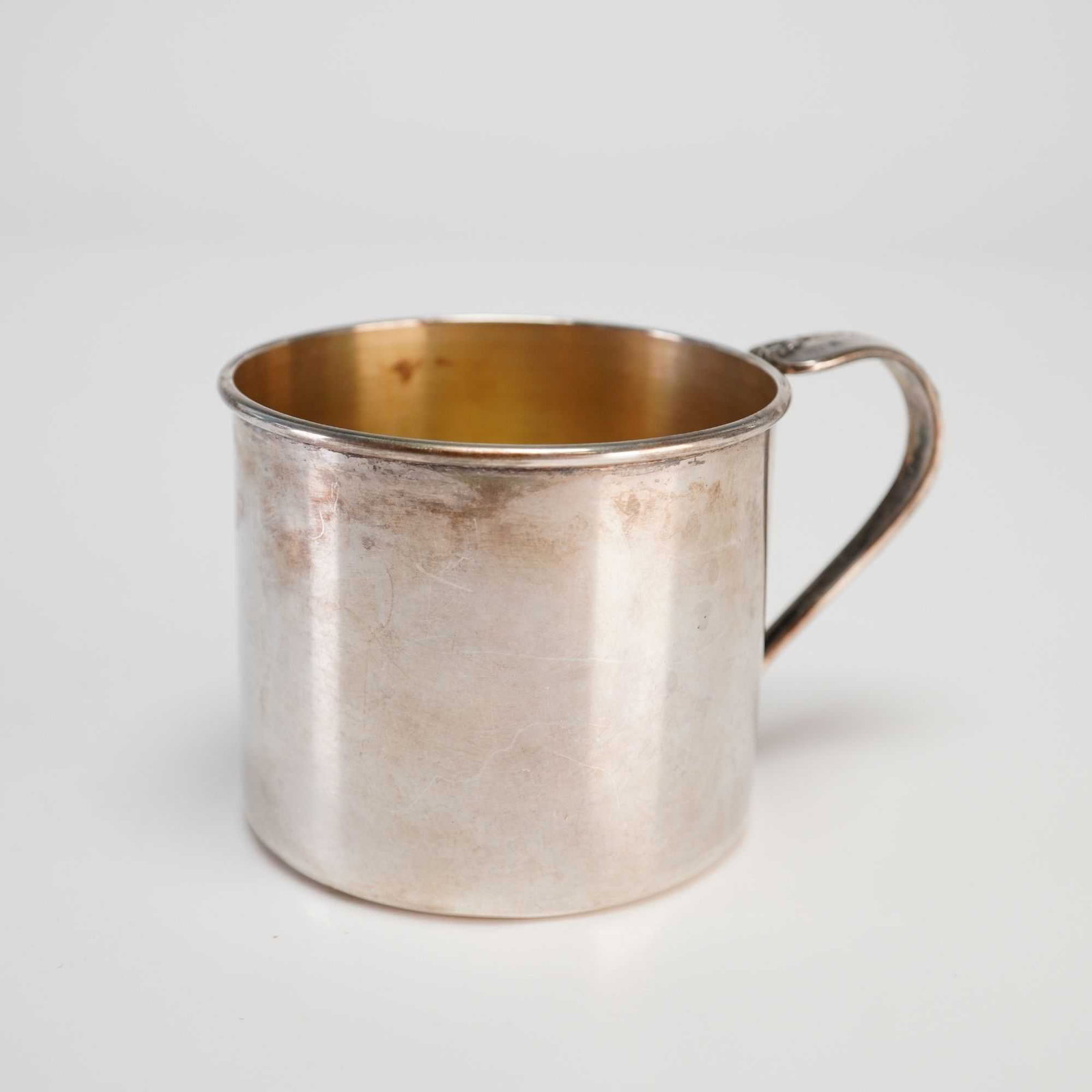 Oneida Community Sterling Silver Baby Cup: This sterling silver child's cup is manufactured by Oneida Community. The vessel is of cylindrical form with a slightly flared rim and features a gold-washed vermeil interior. It is fitted with a