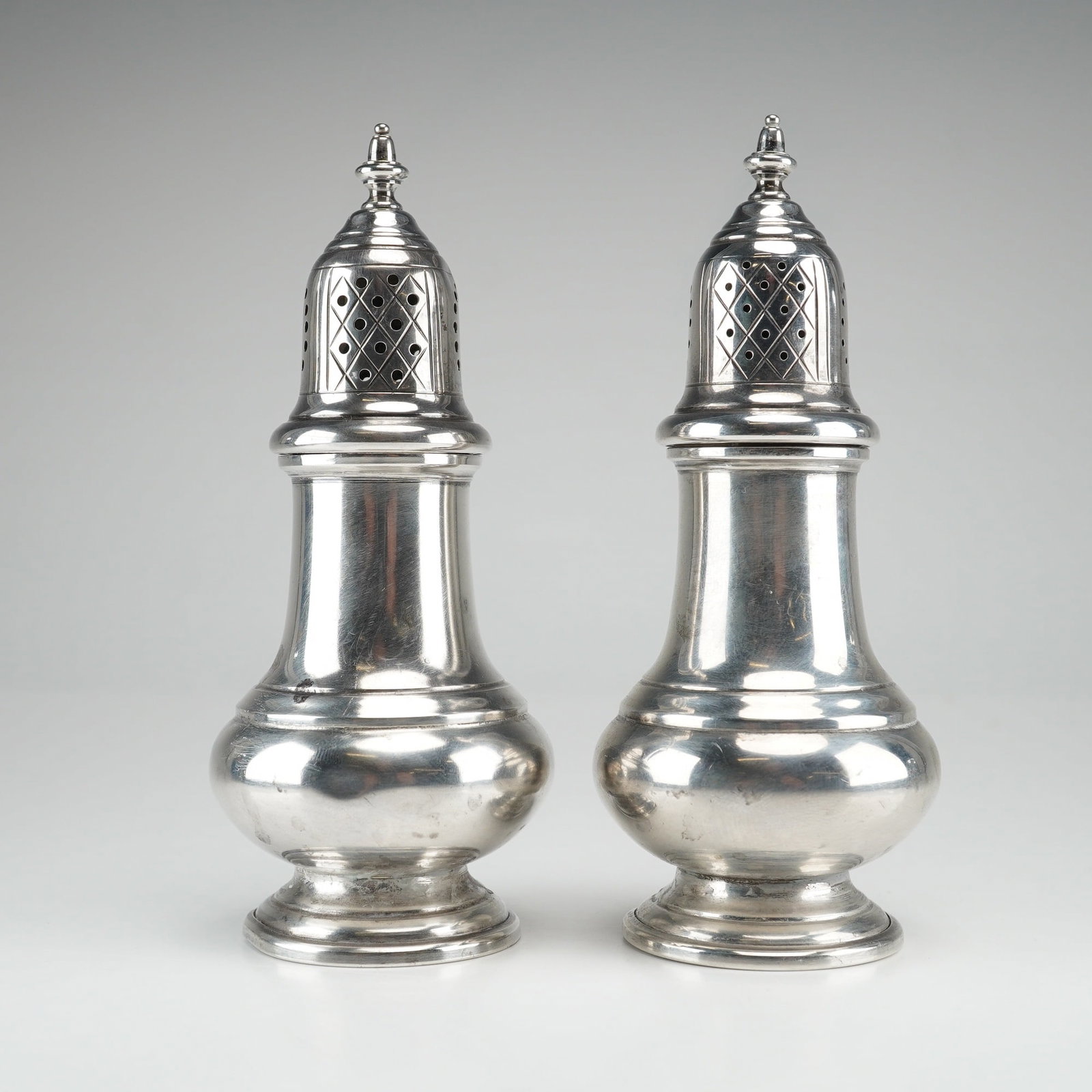 Pair of Gorham Sterling Silver Salt and Pepper Shakers Model 1111: This pair of Gorham sterling silver shakers is identified as model number 1111. Each shaker is designed in a classic baluster form featuring a stepped, circular pedestal base and a waisted neck. The