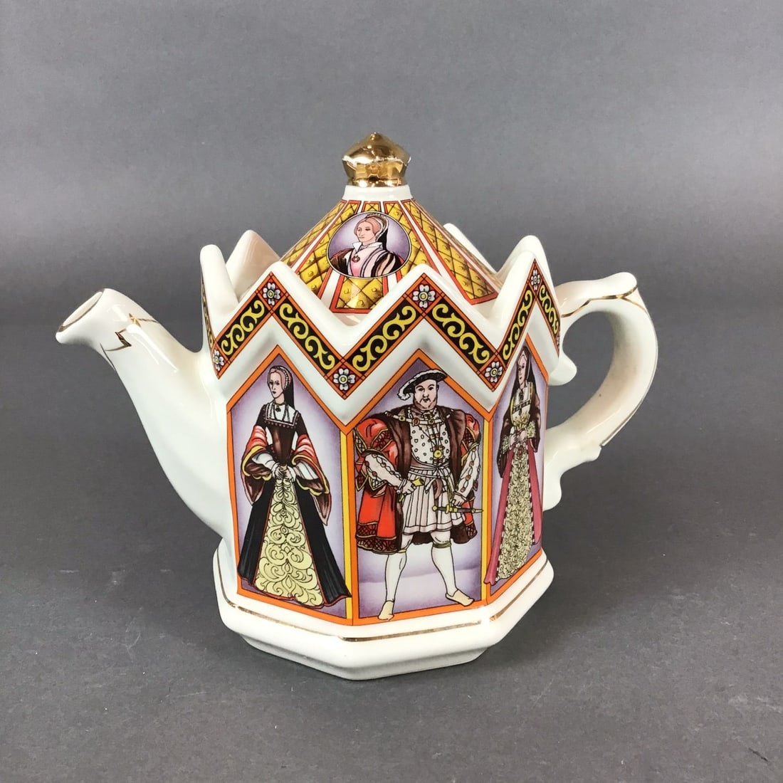 Sadler King Henry VIII and His Six Wives Castle Shaped Teapot with Lid: This Sadler glazed earthenware teapot is decorated in the King Henry VIII and His Six Wives pattern. The piece features a hexagonal body designed in a castle or crown style with a distinctive crenelat