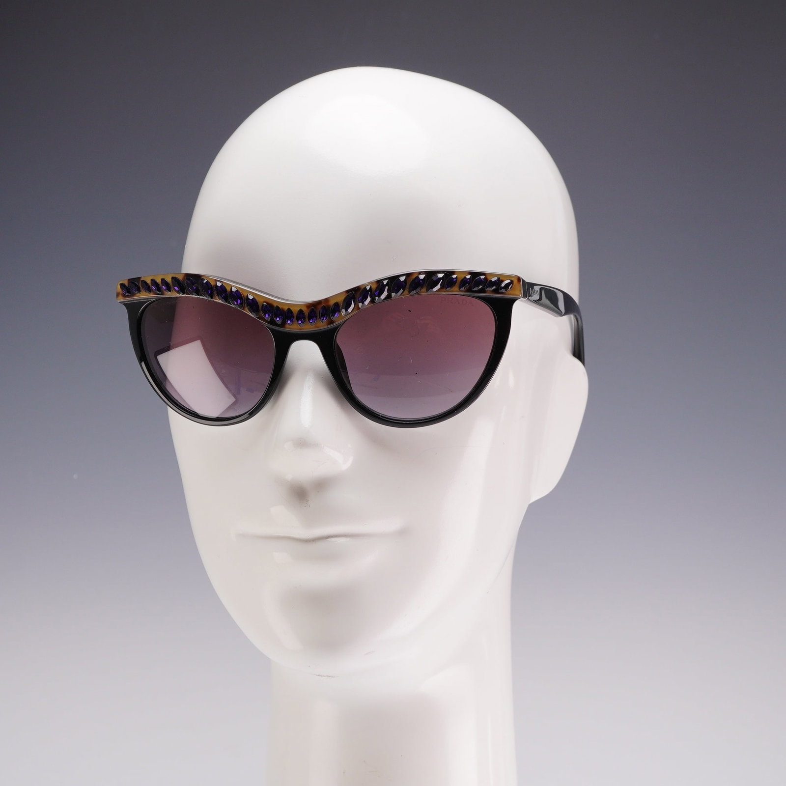 Prada Black with Purple Rhinestone Sunglasses SPR 04P: This lot features a pair of Prada black sunglasses with purple rhinestone accents, model SPR 04P, alongside a collection of writing instrument accessories. The sunglasses are designed with black aceta