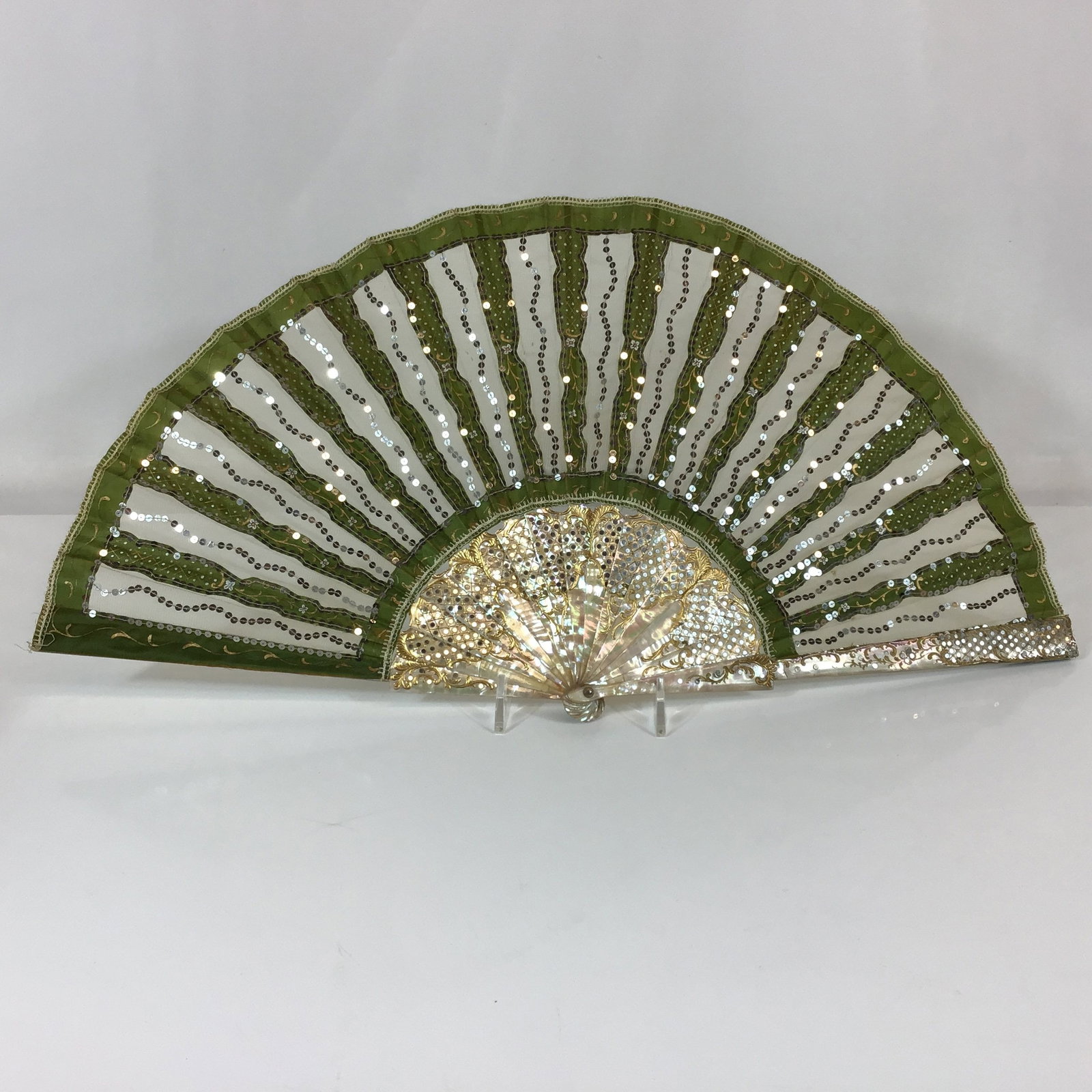 Mother of Pearl and Green Silk Hand Fan with Lace Gauze and Silver Sequins: This folding hand fan features a leaf composed of alternating panels of olive-green silk and translucent gauze lace. The leaf is decorated with vertical, undulating lines of silver-toned sequins or sp