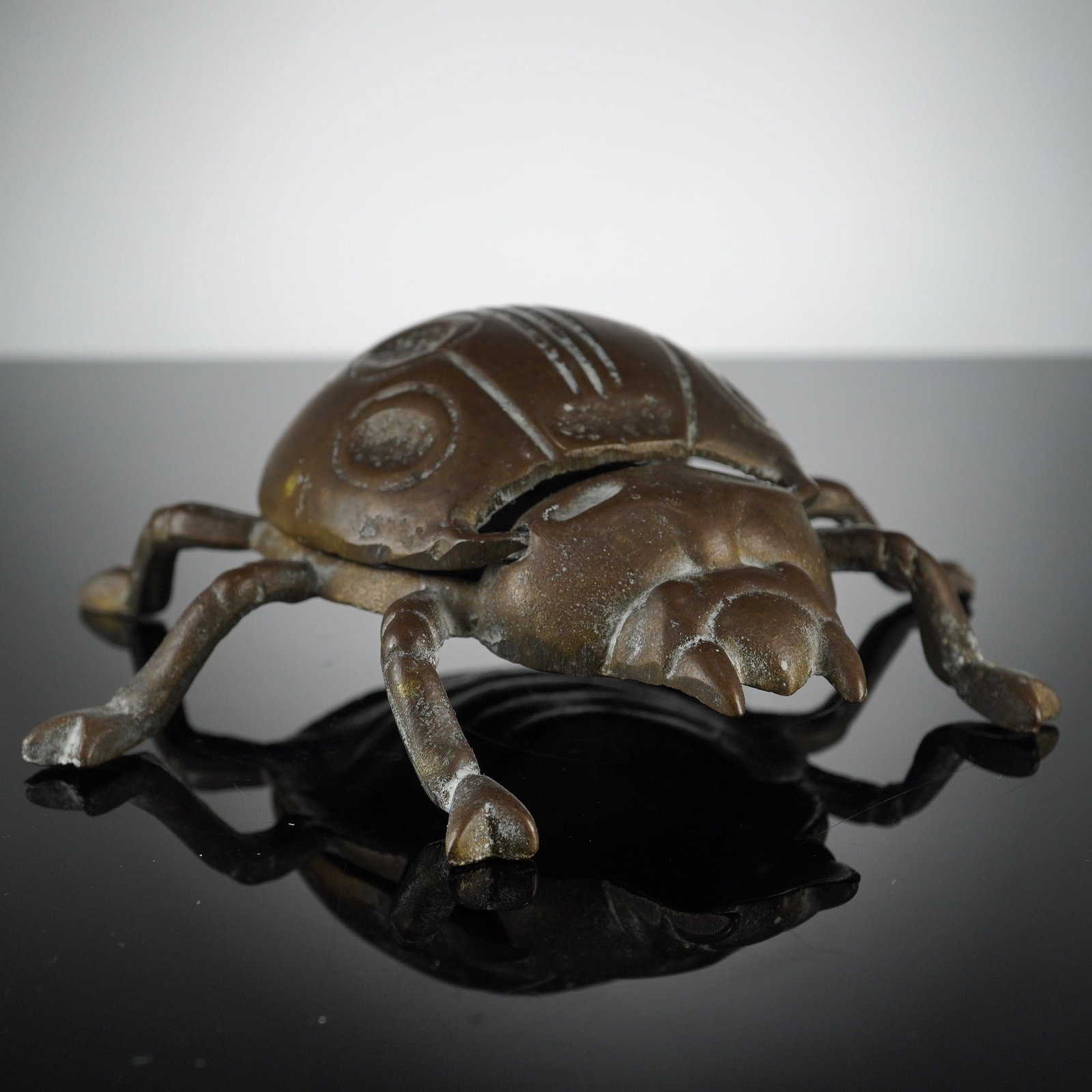 Vintage Cast Brass Beetle Shaped Lidded Ashtray: A vintage novelty brass beetle shaped ashtray, also functioning as a lidded desk or trinket box. The item is constructed of cast brass with a dark brown and bronze-toned patina. The dorsal shell featu