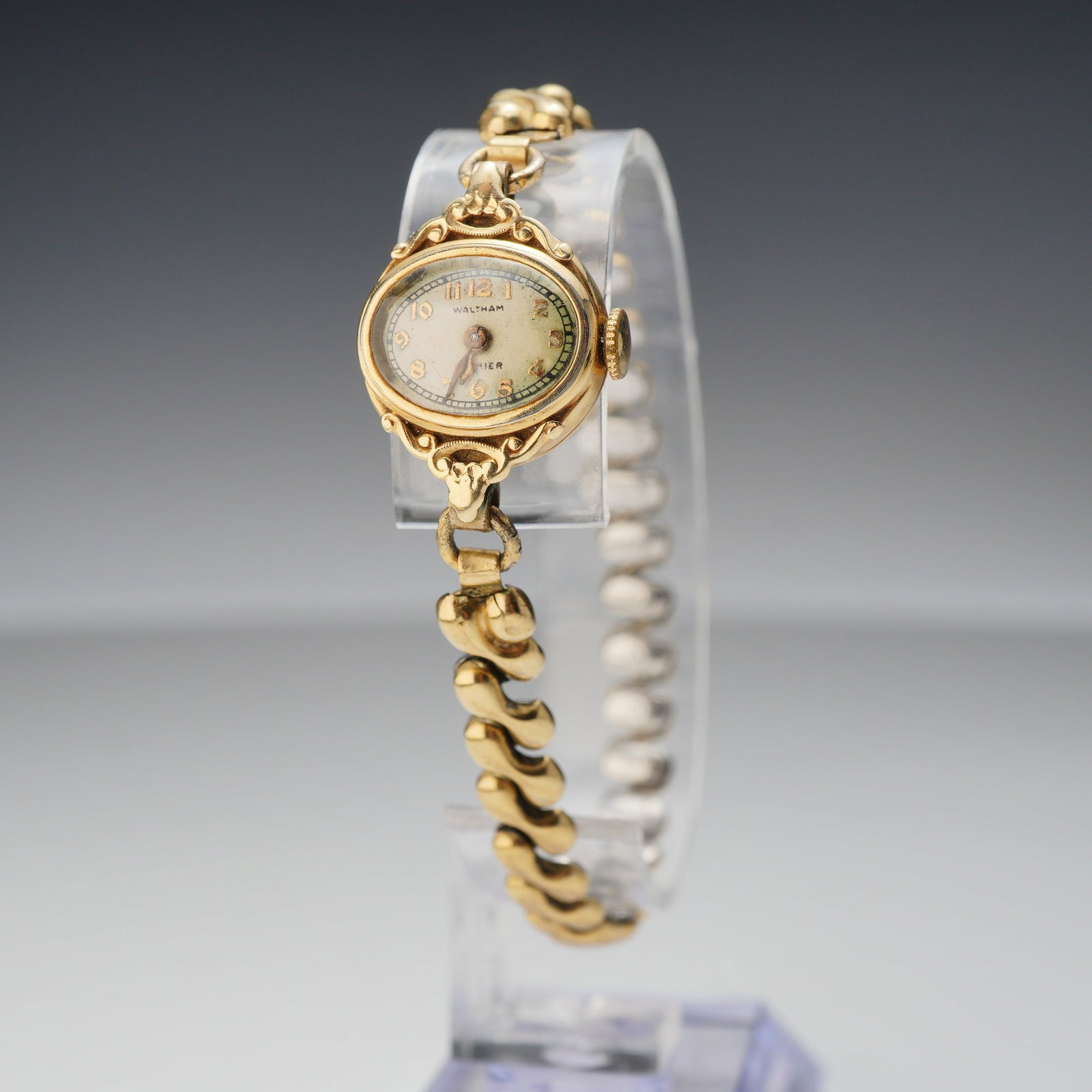 Waltham Premier 9k Gold Ladies Wristwatch: A Waltham Premier manual wind wristwatch featuring a 9k gold case. The petite oval case is designed with ornate scrolling openwork lugs. The cream-colored dial is detailed with applied gold-tone Arabi