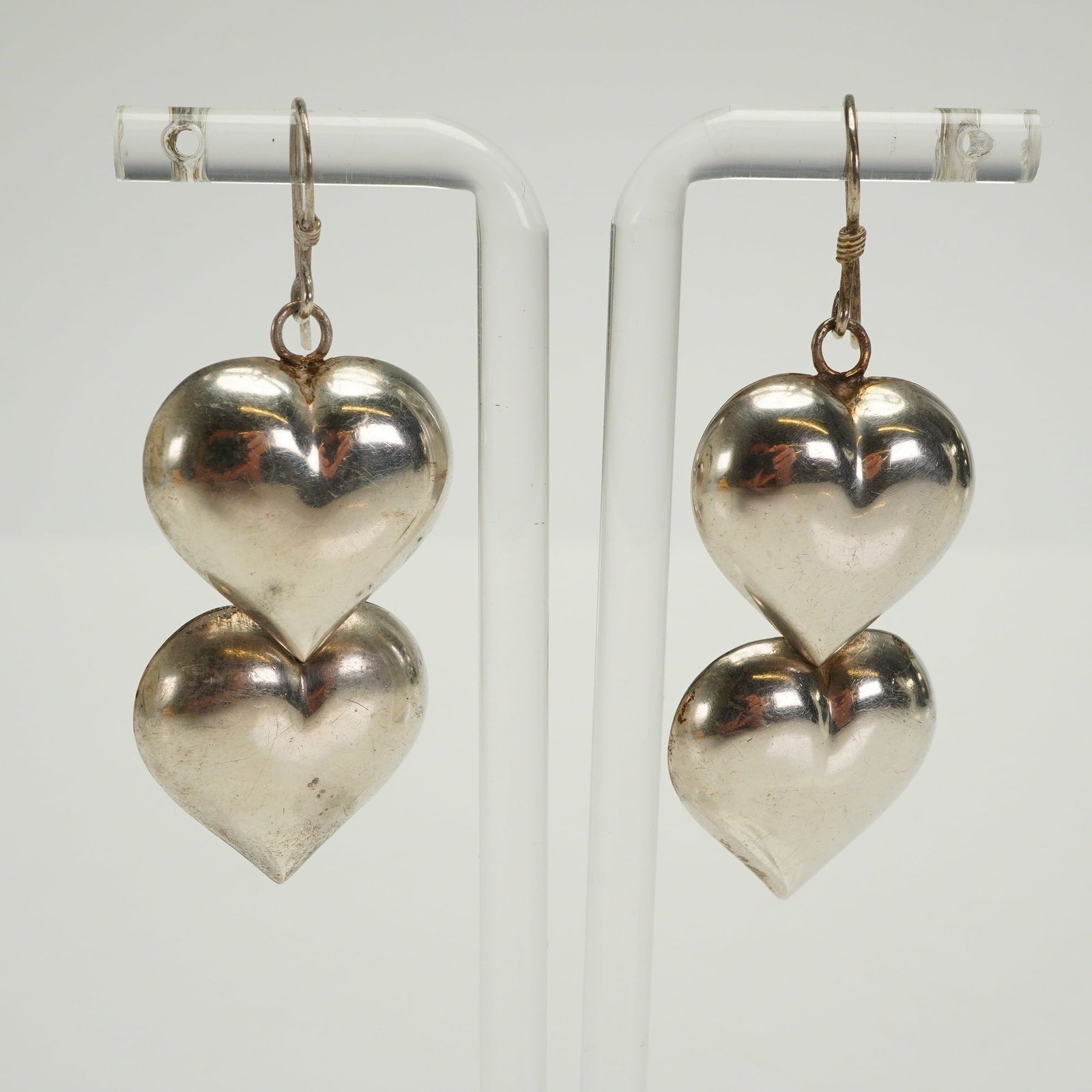 A Pair of Modernist Sterling Silver Heart Earrings: A pair of sterling silver dangle earrings crafted in a Modernist style. Each earring features two vertically stacked, puffed heart components connected by jump rings and suspended from simple French w