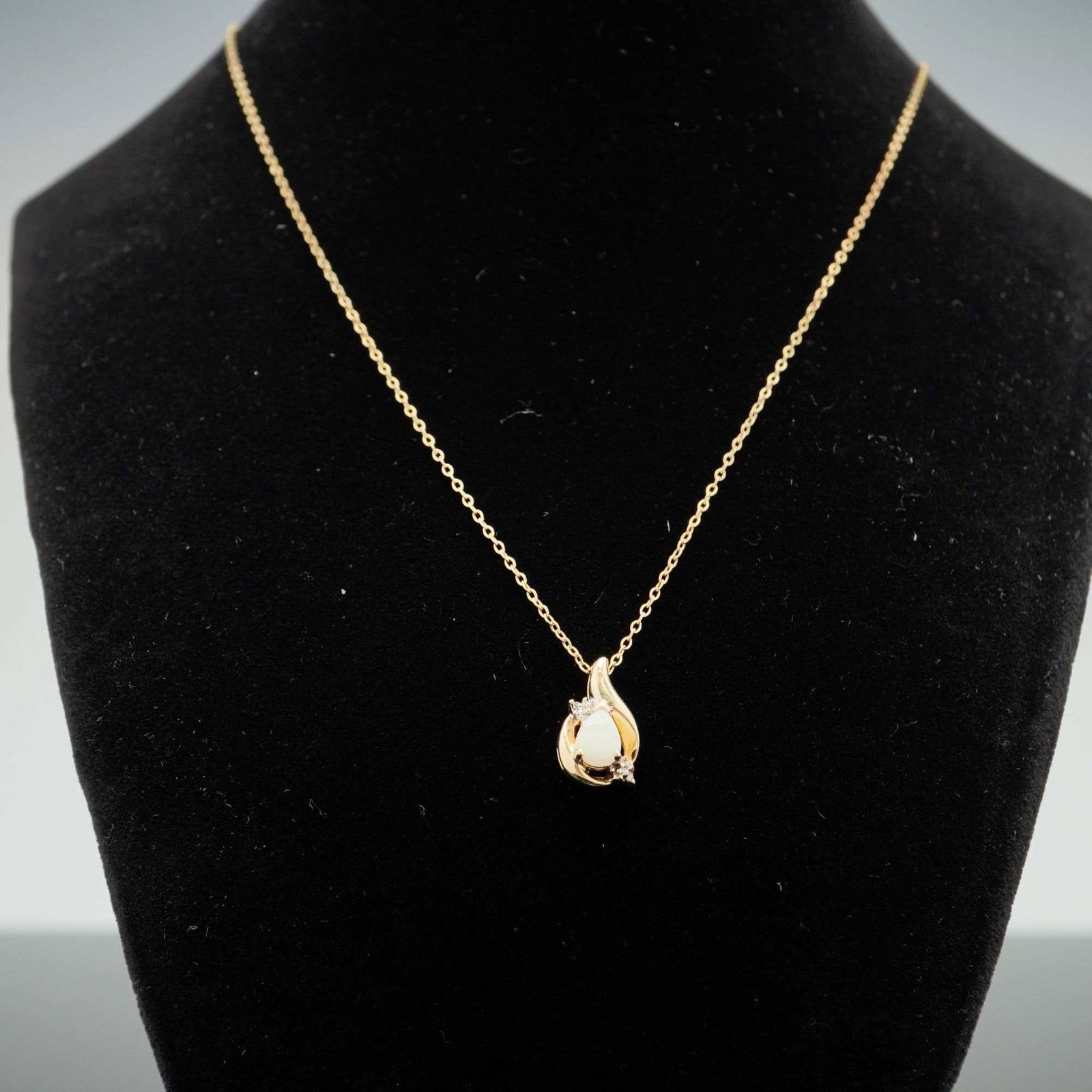 14K Yellow Gold Pear-Cut Opal and Diamond Swirl Pendant Necklace: A 14 karat yellow gold pendant necklace featuring a central pear-cut white opal cabochon. The opal exhibits green flashes of play-of-color and is secured in a multi-prong setting. The pendant frame fe