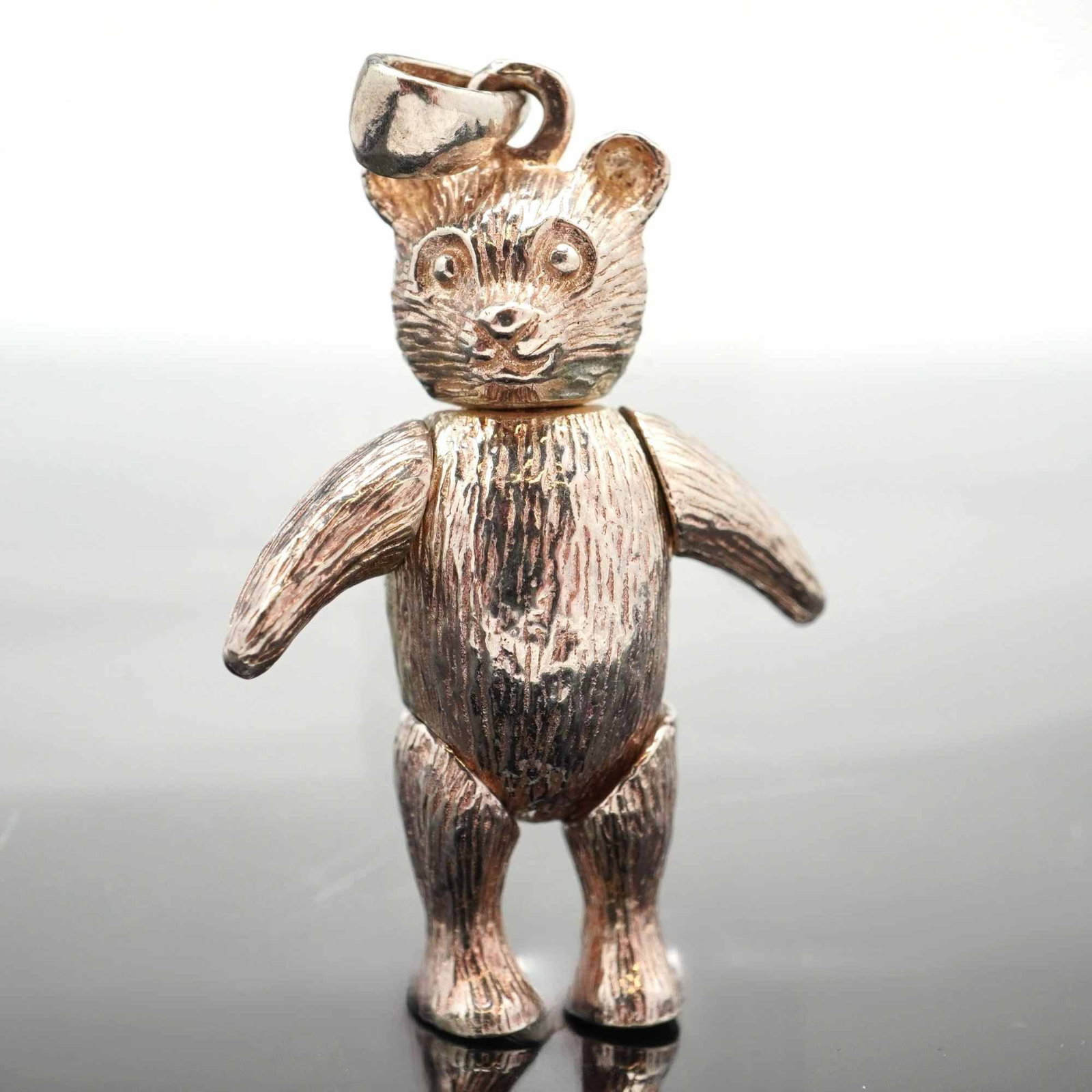 Sterling Silver Articulated Teddy Bear Pendant: This is an articulated teddy bear pendant crafted from sterling silver. The figure is designed with five points of articulation, allowing the head, arms, and legs to move independently. The surface of