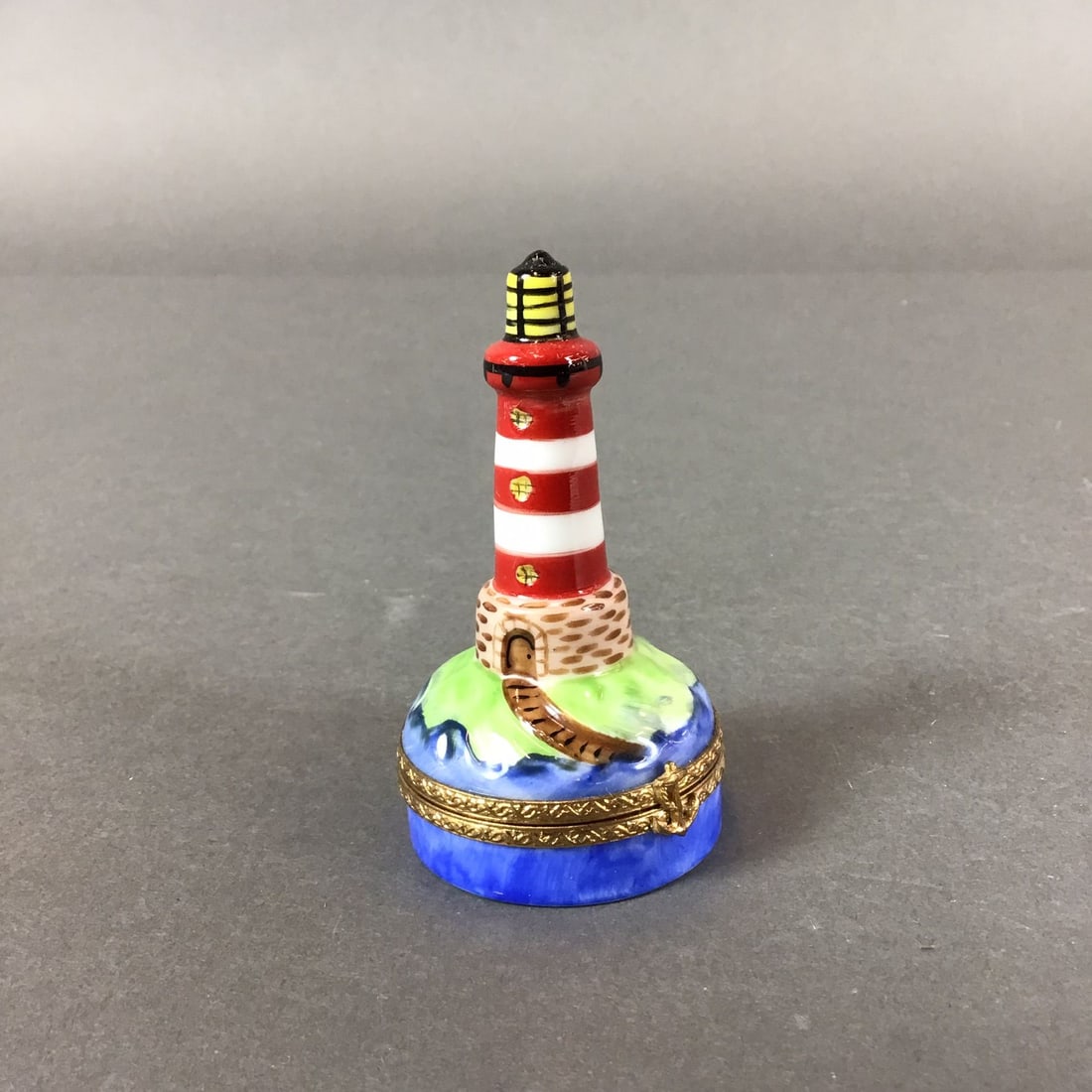 Limoges France Limited Edition Porcelain Lighthouse Trinket Box: This hand-painted porcelain hinged trinket box is produced in Limoges, France, and is fashioned in the form of a lighthouse featuring a red and white striped tower with a yellow lantern room at the pe